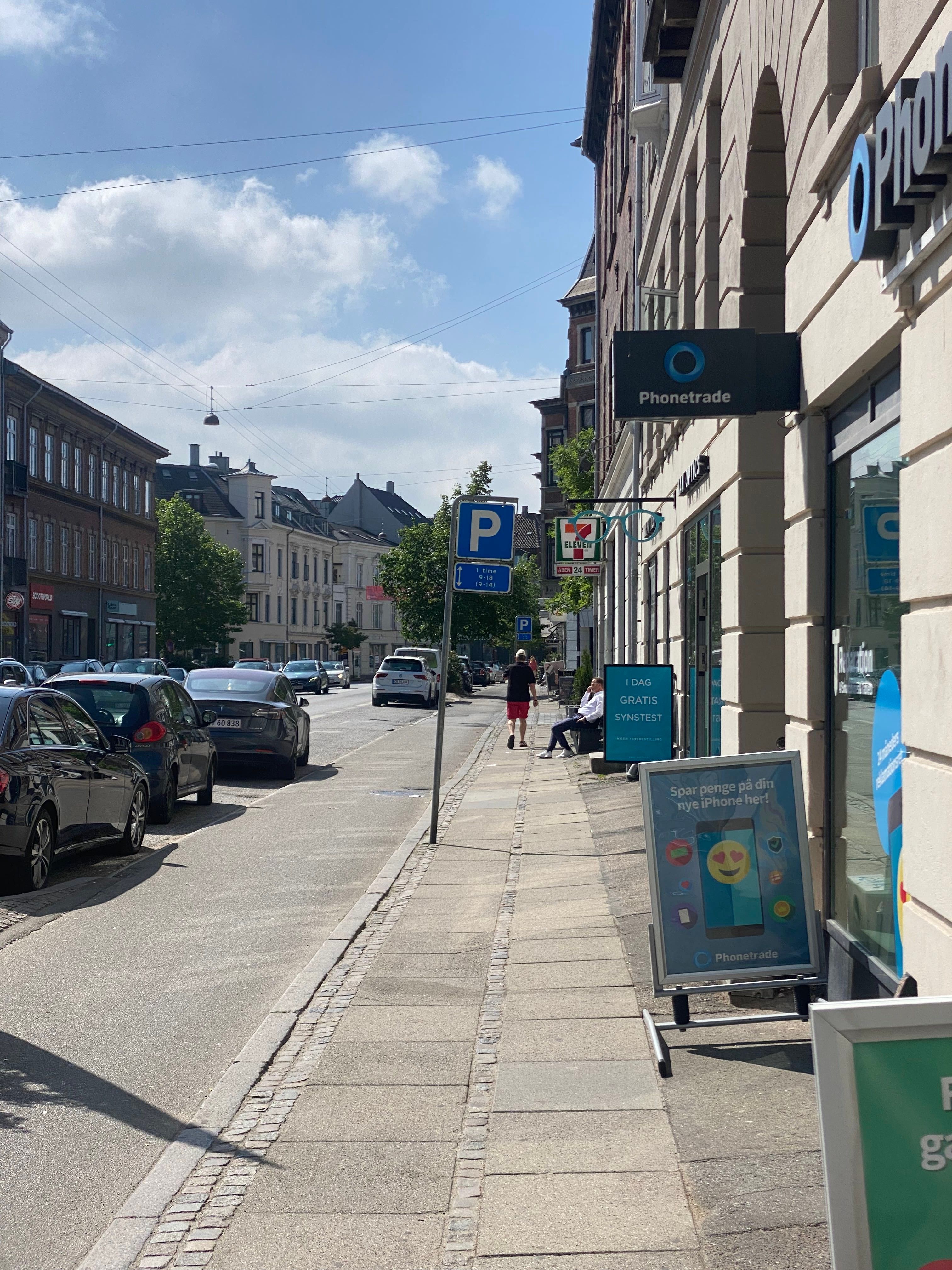 Parkerede biler langs gaden med Phonetrade-skilt og en mand, der går med rødt t-shirt og bukser