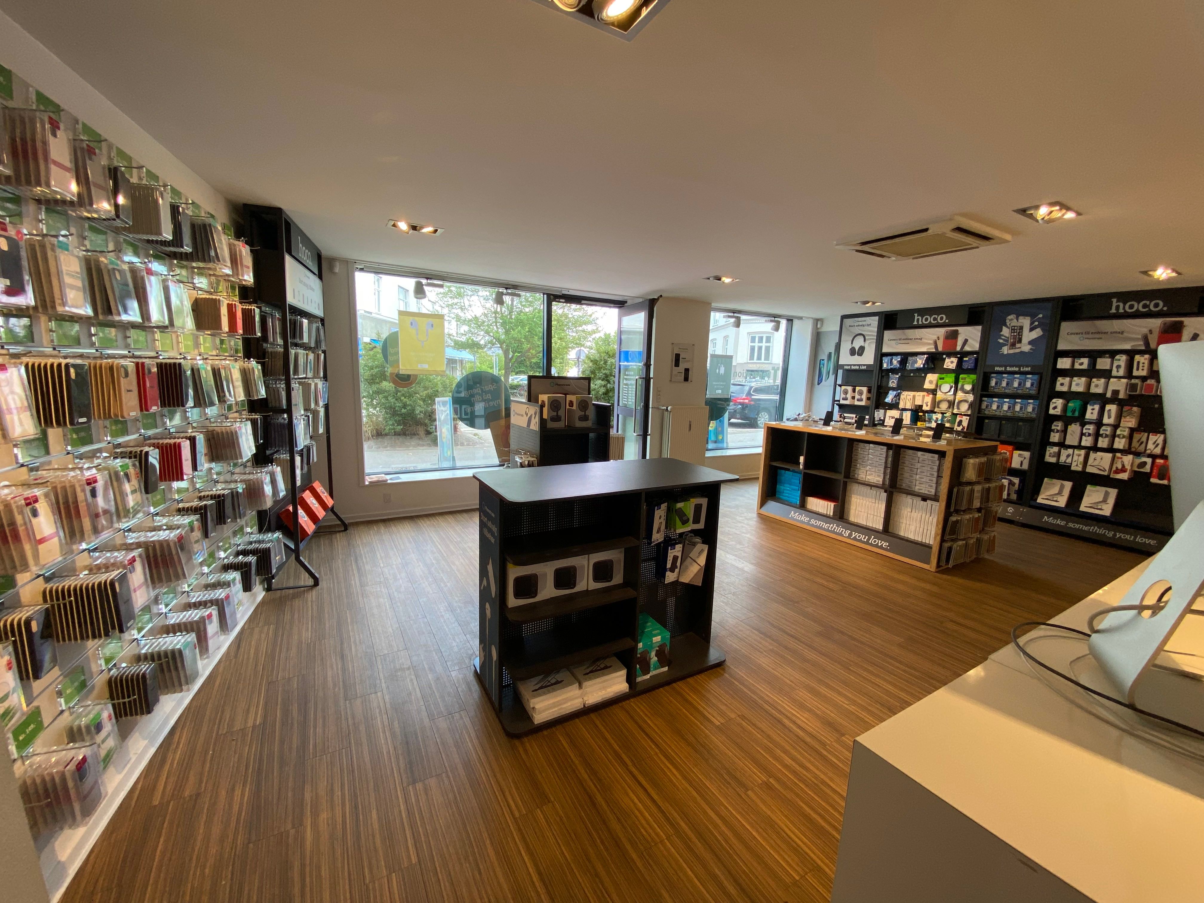 Forretningslokal med flere hylder med elektronik og gadgets og trægulv. Foran er et skrivebord med flere ting, og på højre