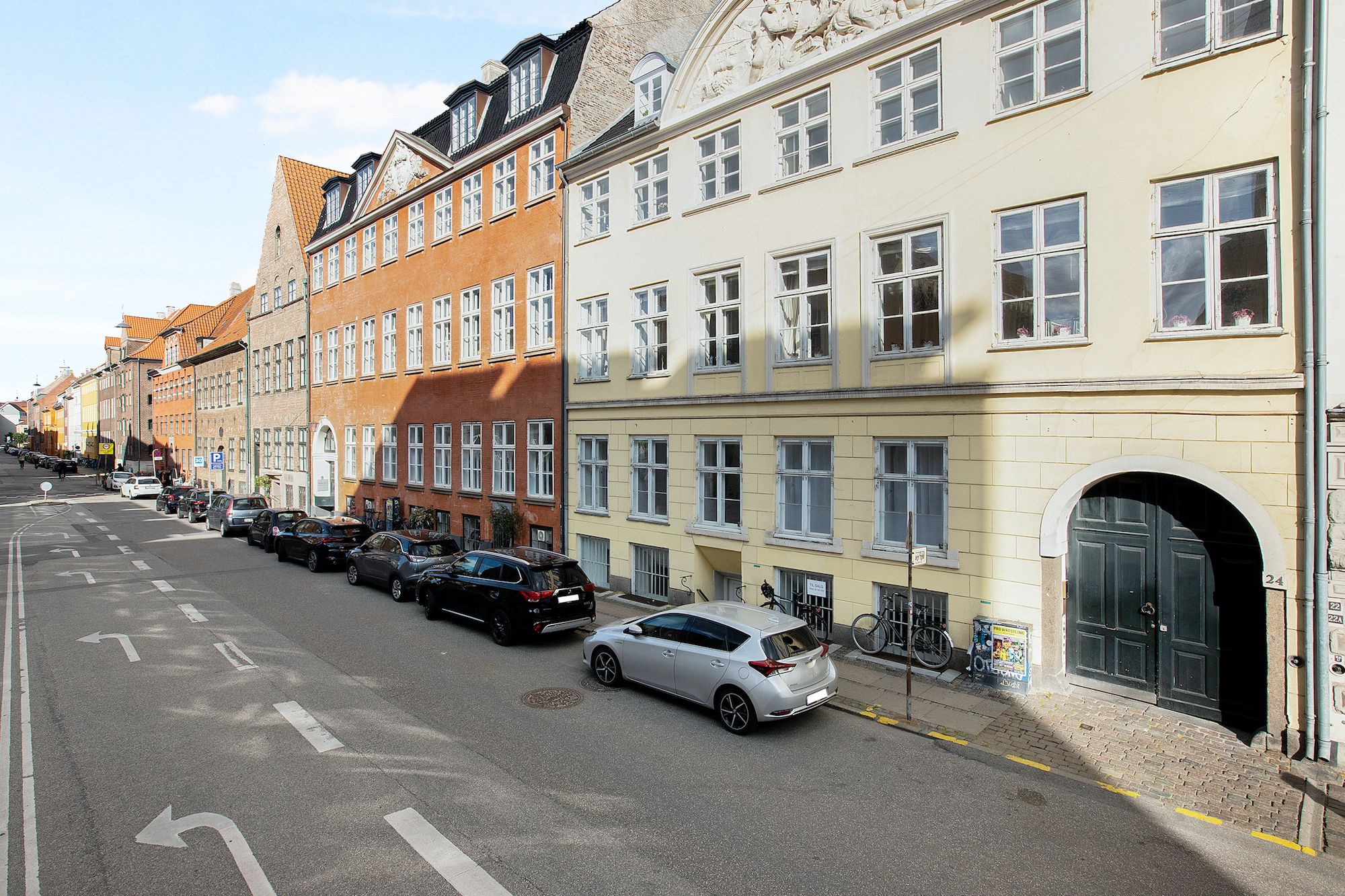 En lille gade i København med parkerede biler og en gågade med gamle bygninger med røde tag og store vinduer