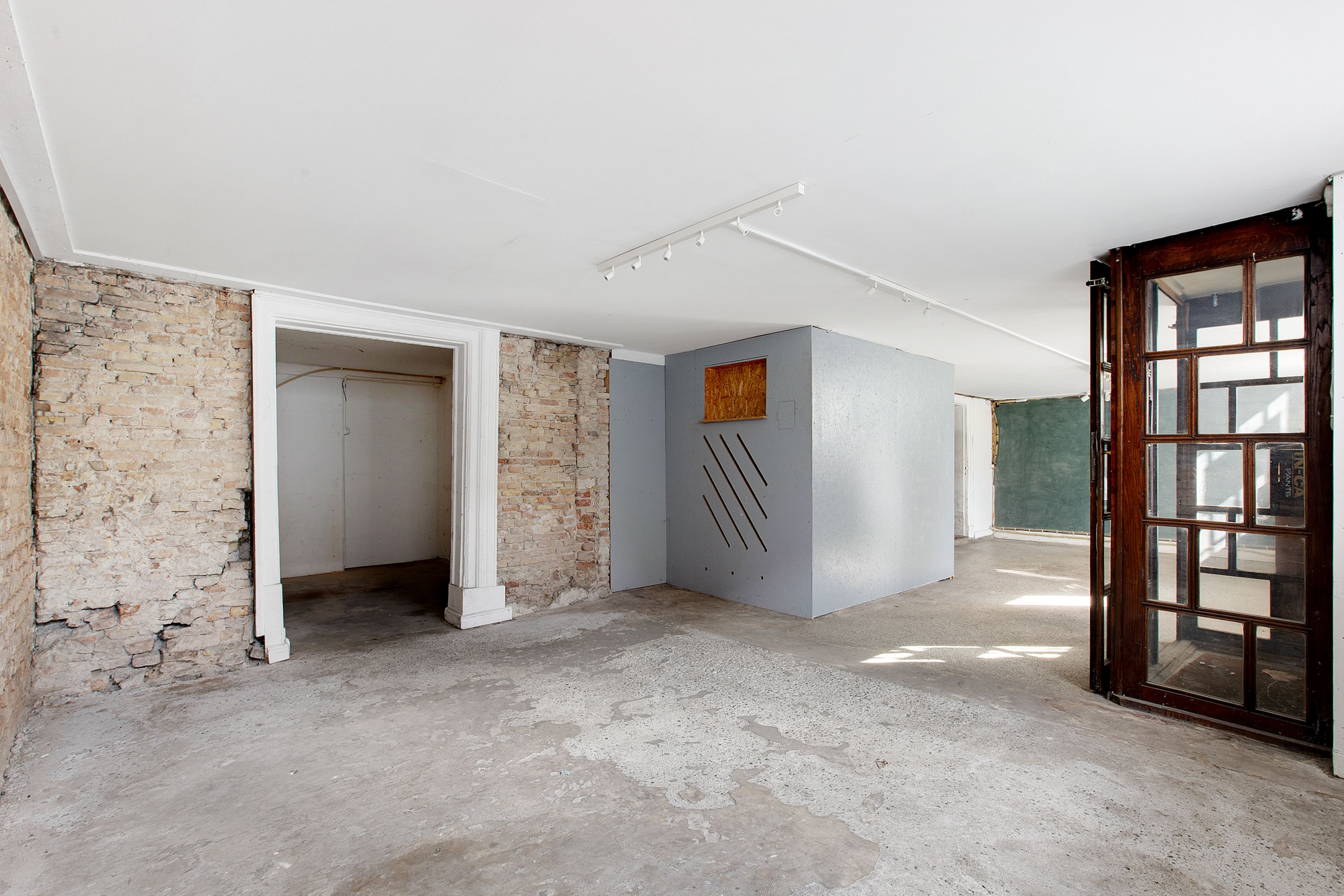 Tomt rum med stenmur, cementgulv og åbent trædør. Loftet er hvidt med indbygget lys og trægulv.