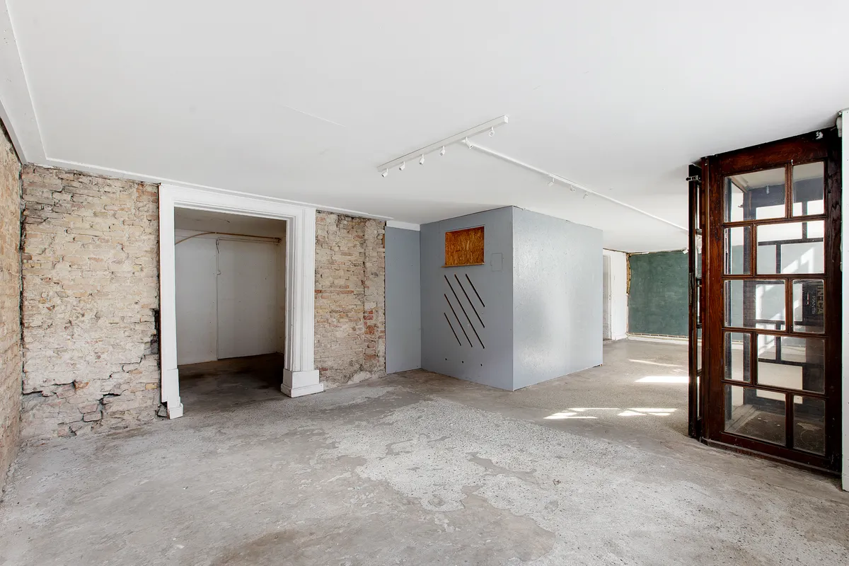 Tomt rum med stenmur, cementgulv og åbent trædør. Loftet er hvidt med indbygget lys og trægulv.