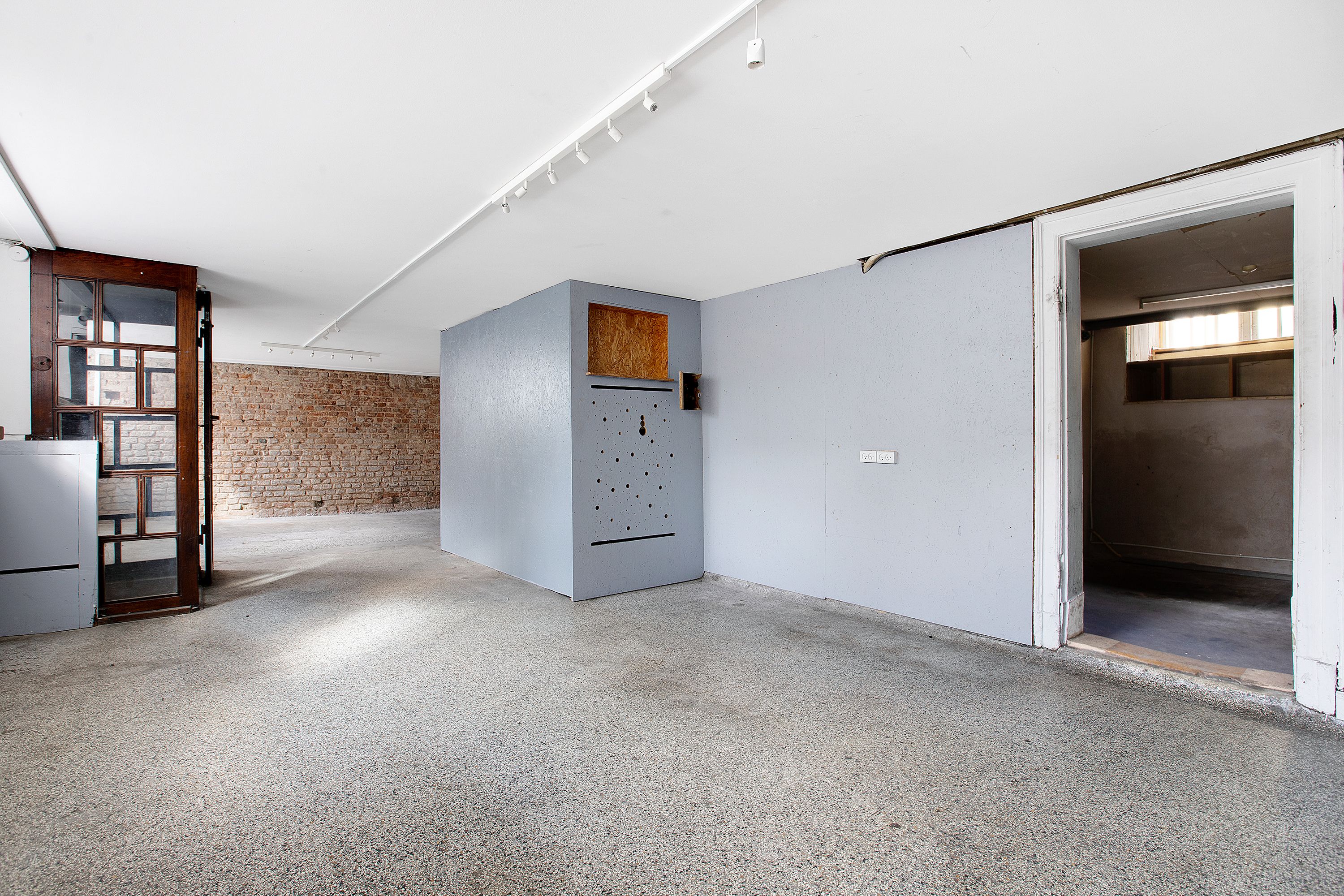 Rum med højt loft og lys gulv og vægge, en gammel dør og et hul i væggen