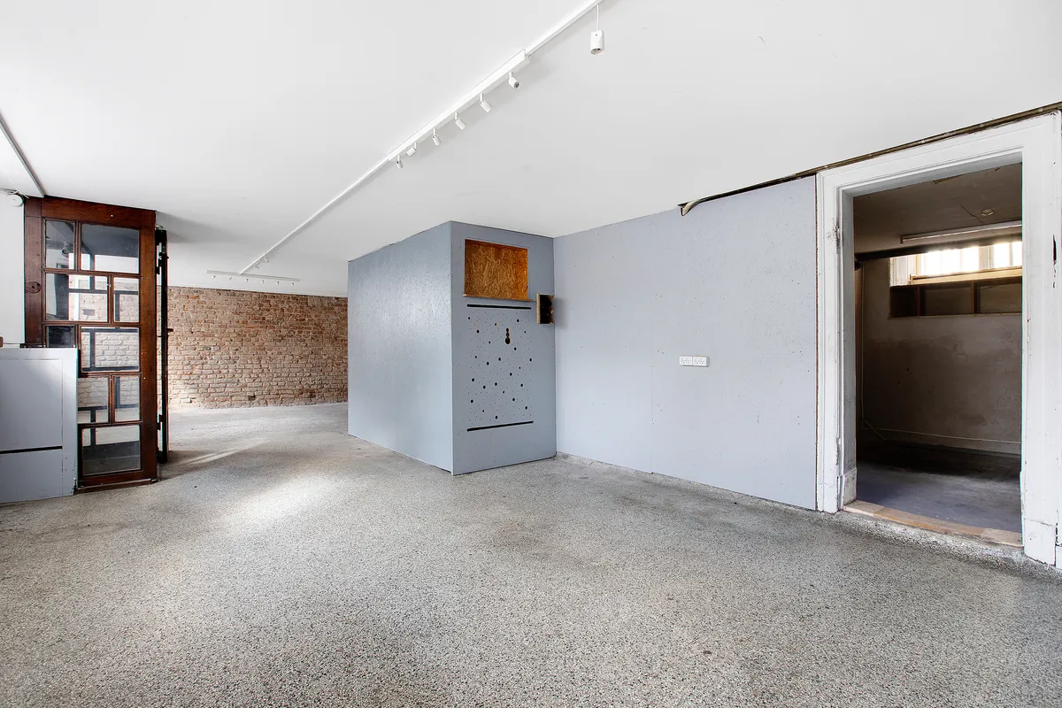 Rum med højt loft og lys gulv og vægge, en gammel dør og et hul i væggen