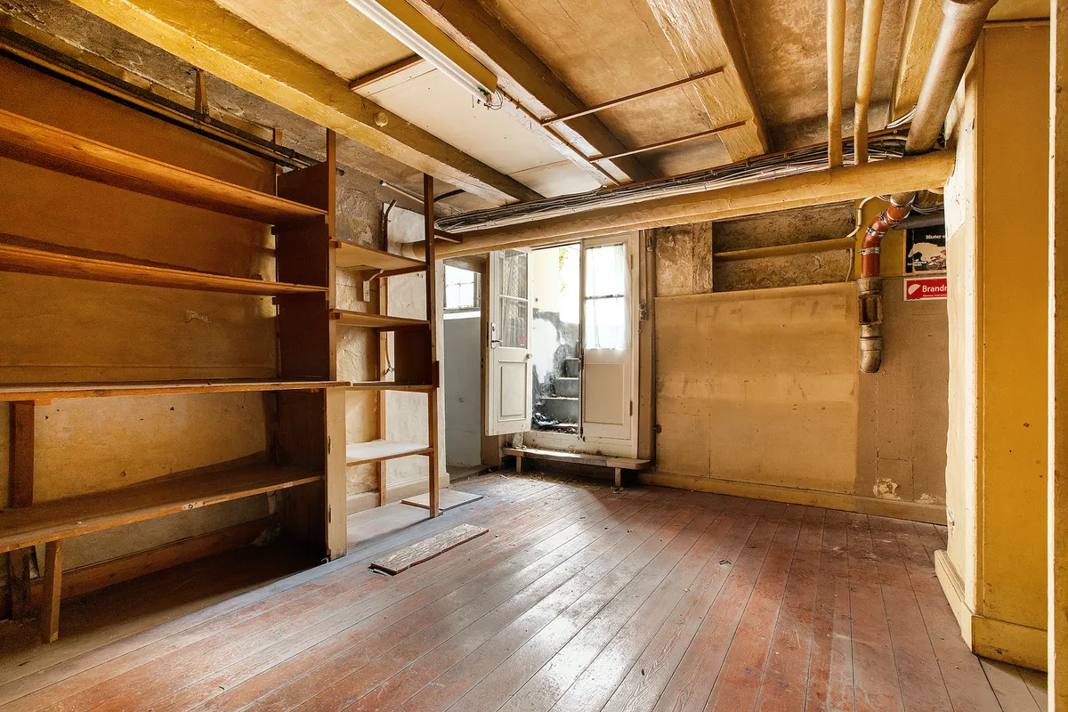 Et stort rum med lysegul væg og lysegul loftsbjælke, åbne døre og lysegul gulvplanke samt lysegul bjælke med rør og metalrør