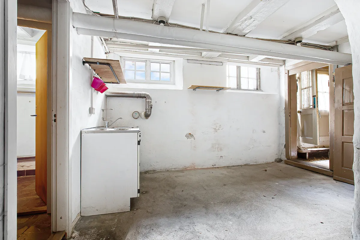 Et køkken med vaskebækken og køleskab samt røret og ventiler på væggen samt åbne døre til udendørs og vinduer med udsigt til