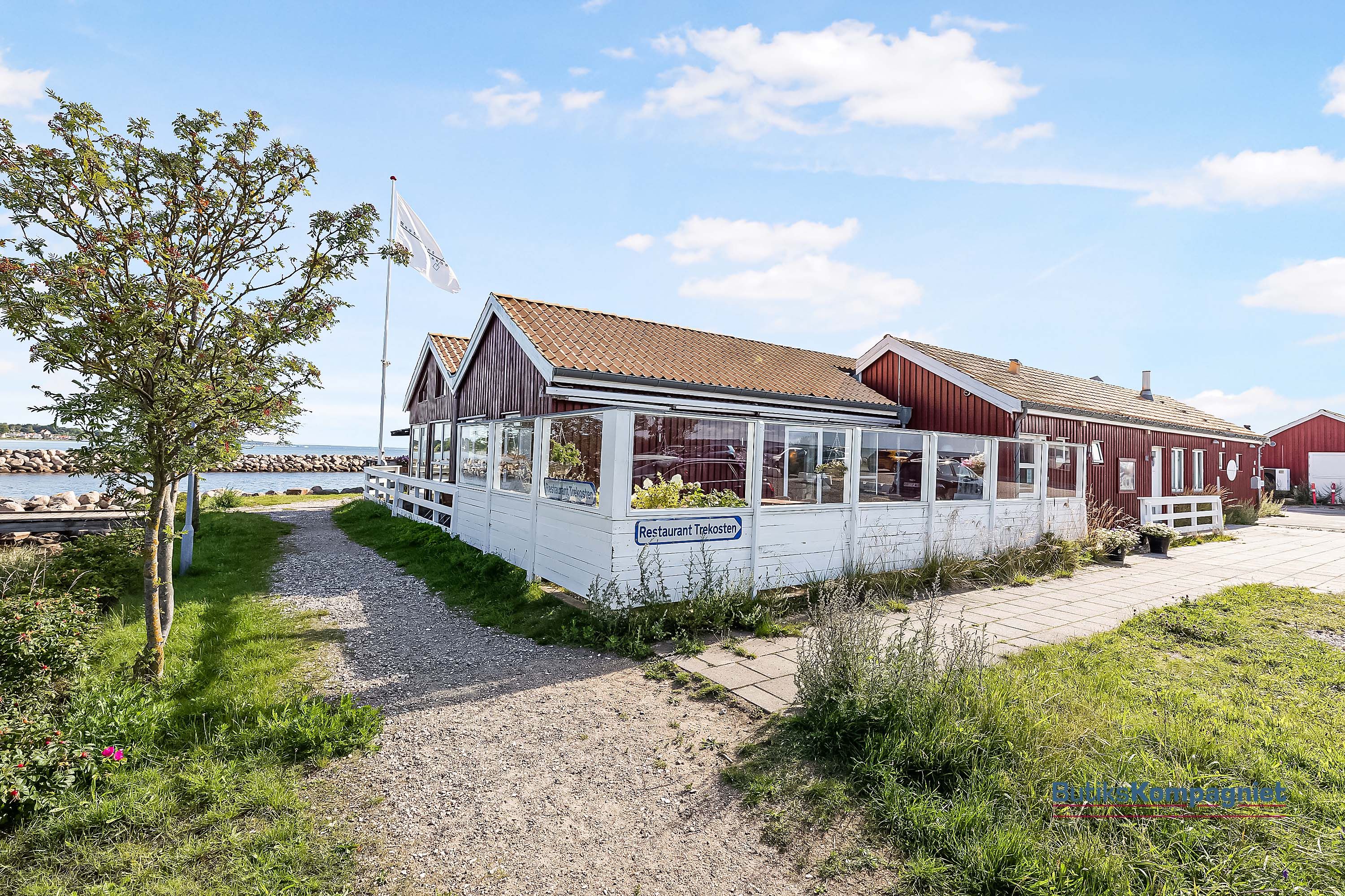 En rødmalet bygning med en terrasse og glasvinduer ud til vandet i Nivå Havn