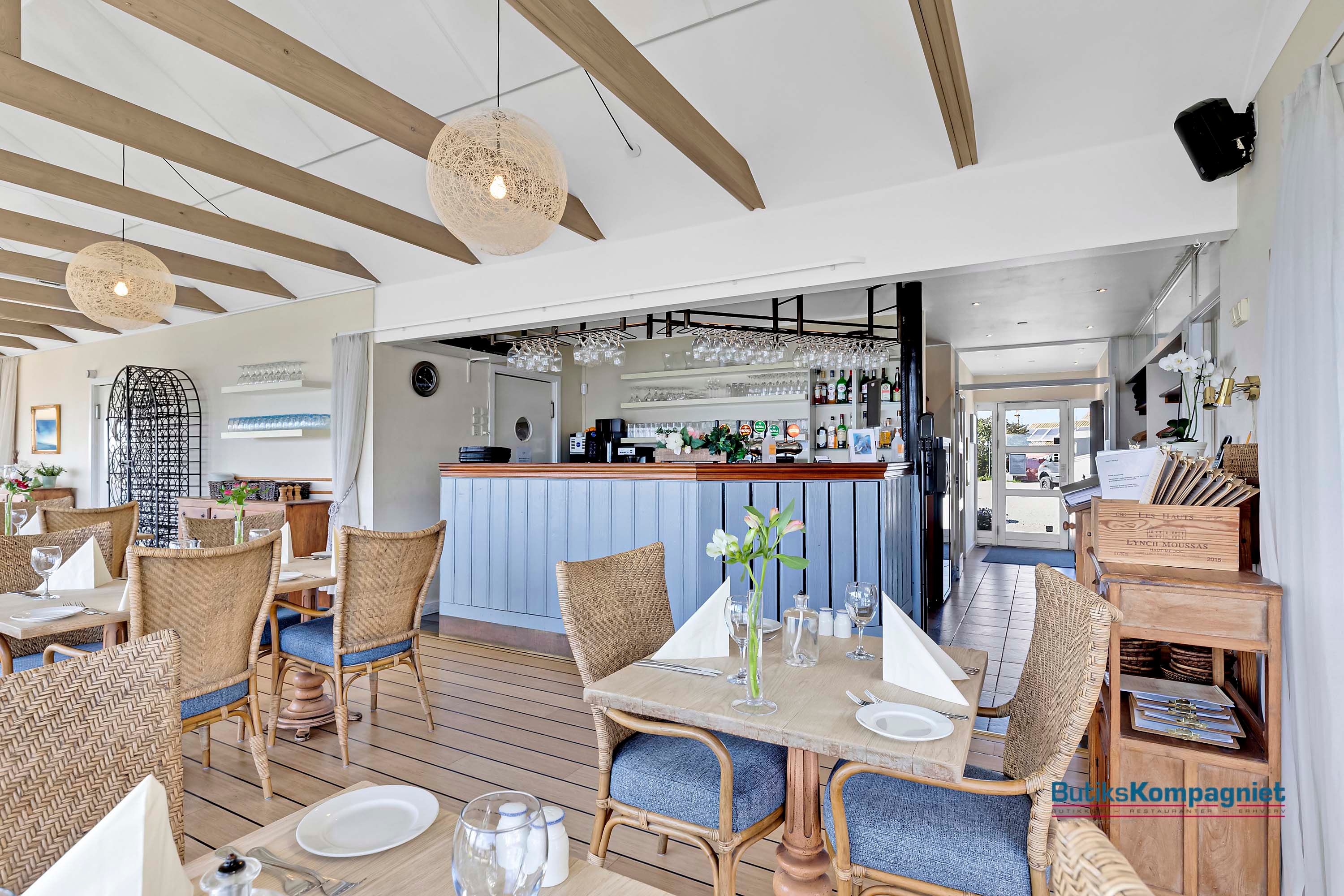 Et søjleforsyningsbord og flere stole med glas og serveret bord er i restaurant med højt loft og træbrædder.