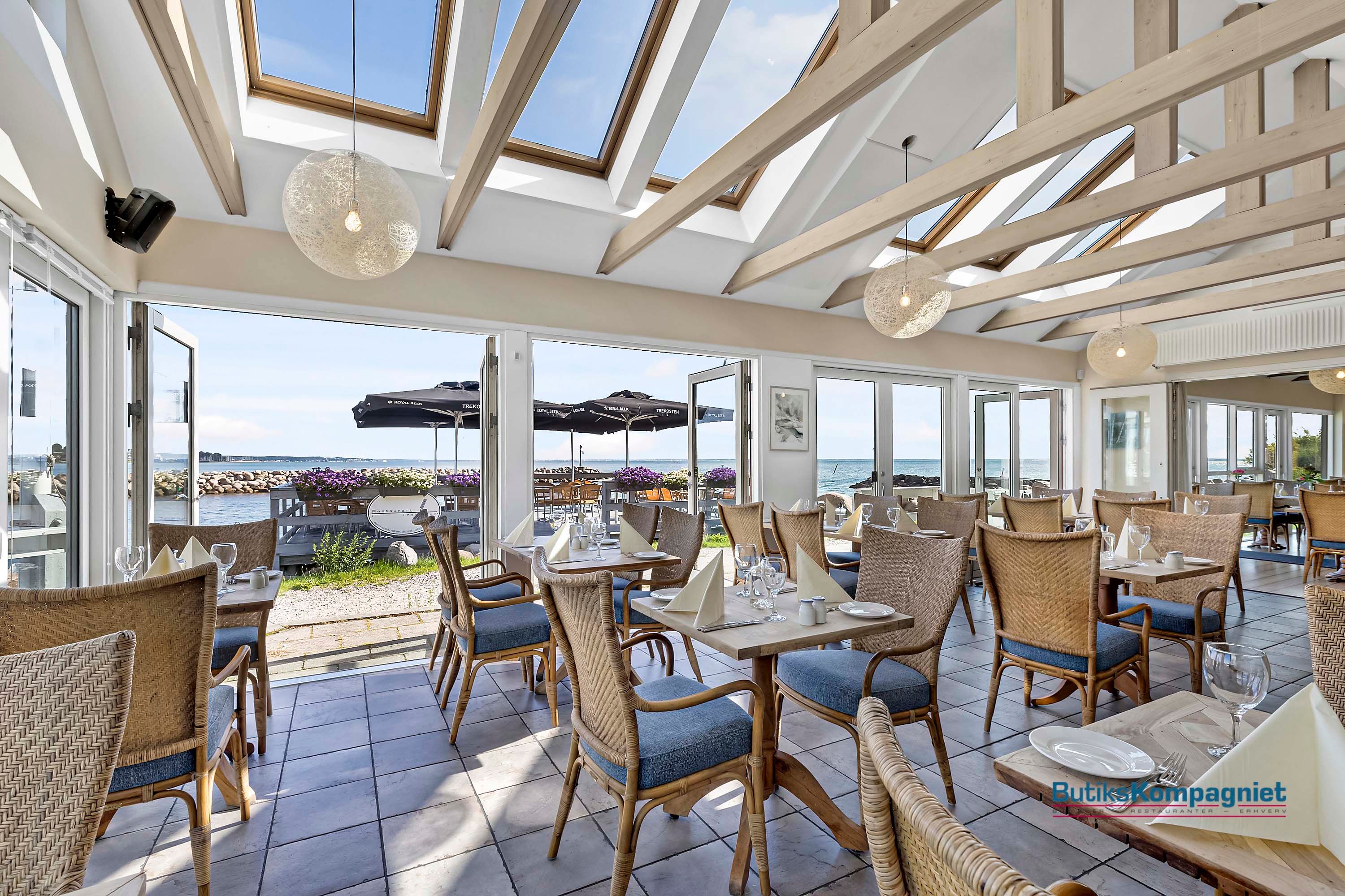 Lys, hyggeligt restaurantindretning med havudsigt, lyse loftsbjælker og solskinsreflekser på gulvet og træborde