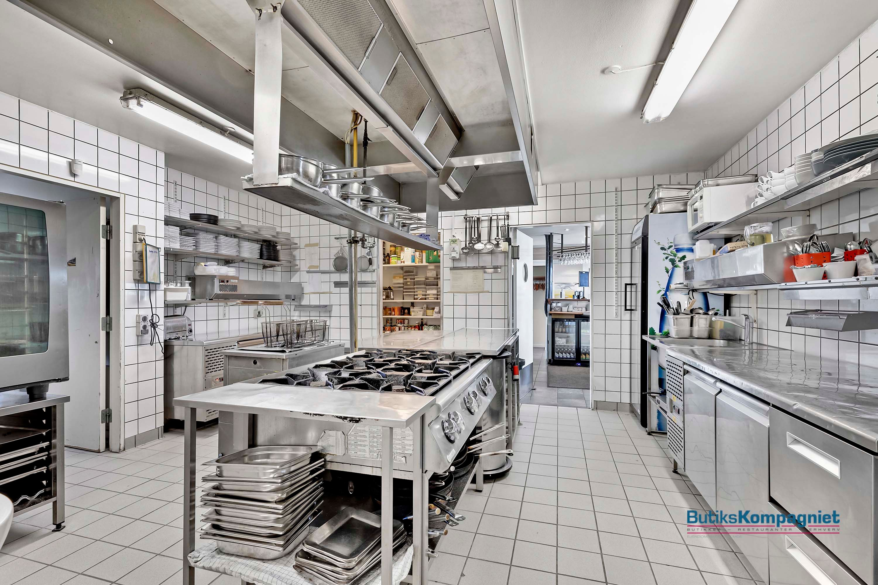 En stor kommerciel køkken med flere kogeapparater, ovne, køleskabe, og udstyr placeret i et rektangulært rum med smukke