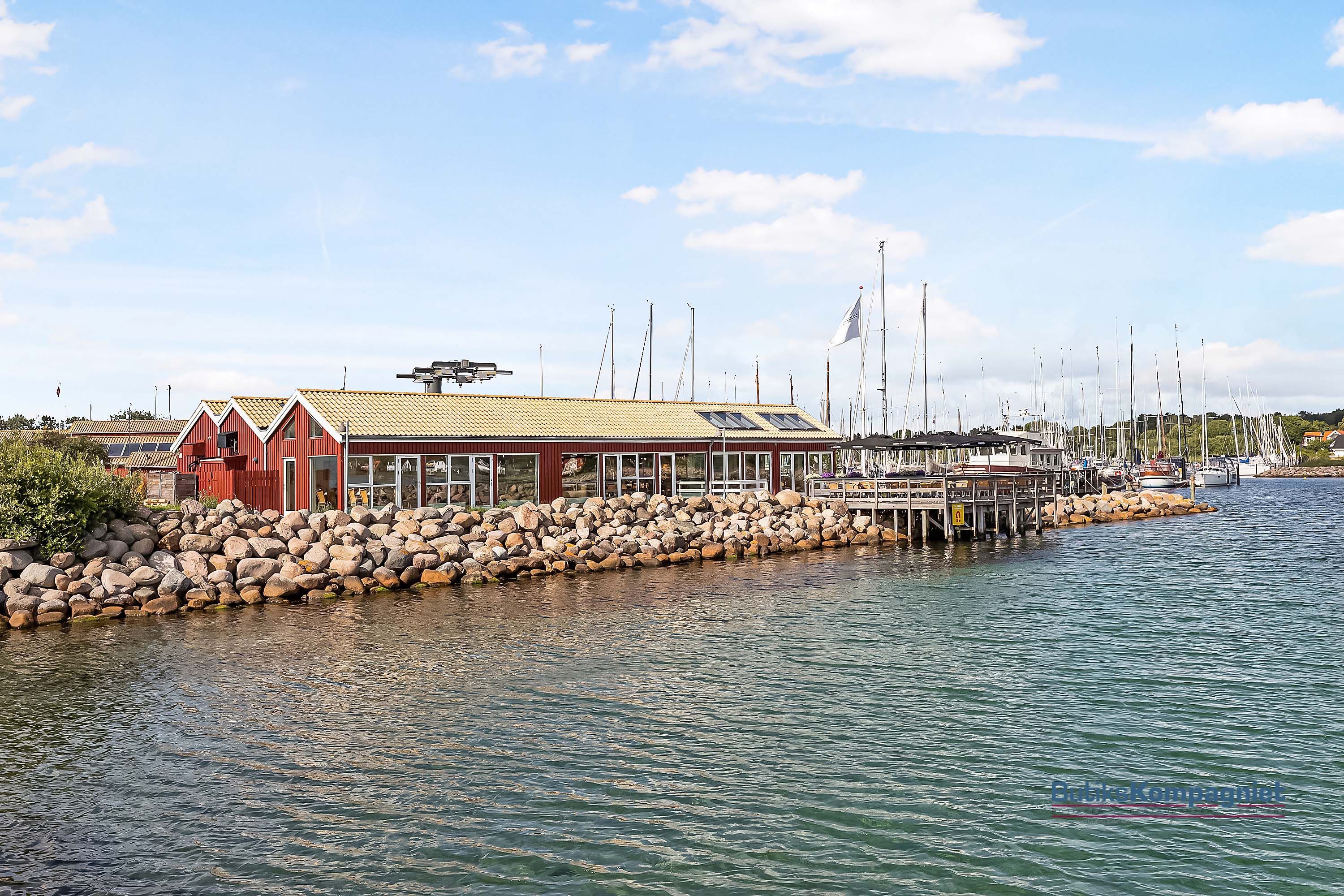 Nivås havn med solceller på rødt hus, flere søjler og både, samt havnens sten og sømærke
