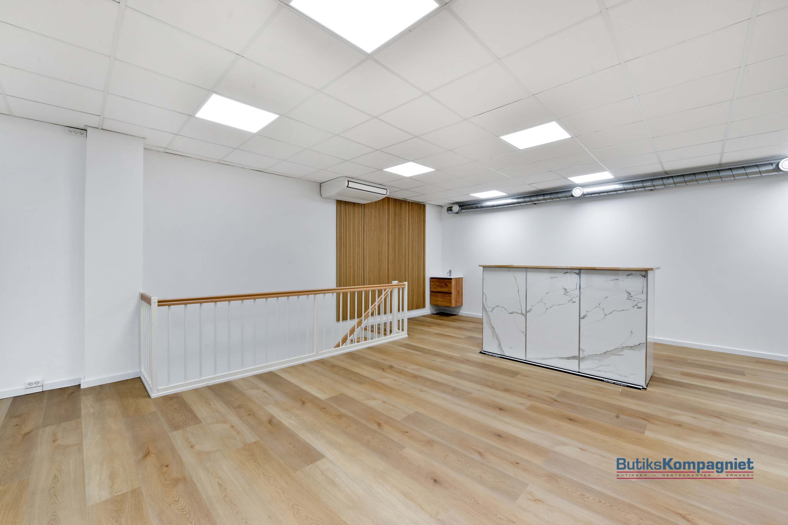 Et møbleret lokale med marmor og træelementer, hvide vægge og loftsbelægning samt trægulve og en hvid trappe med træhåndtag