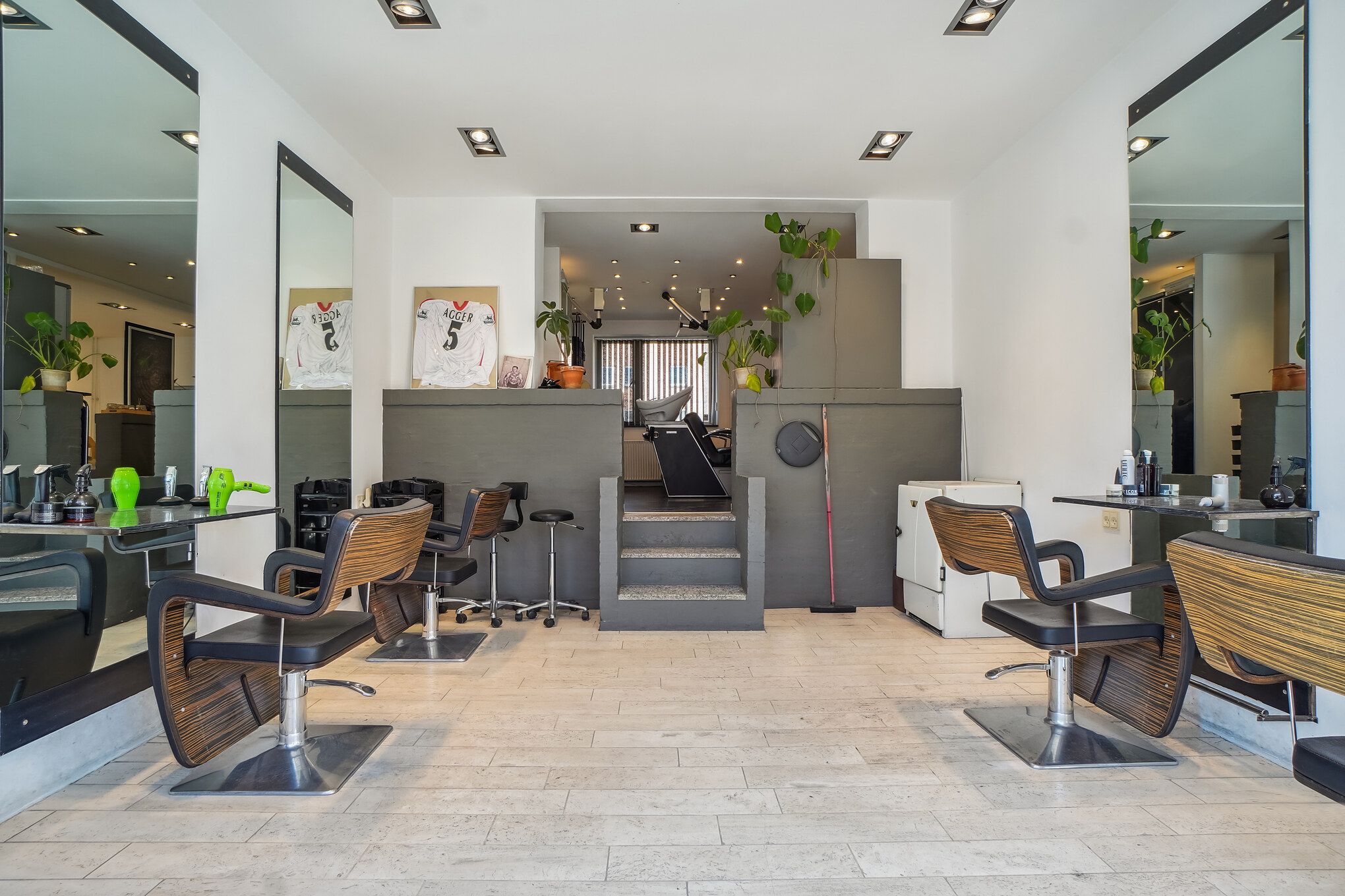 Frisørsalon med moderne barberstole og lyse vægge samt spejle og plante i terrassen