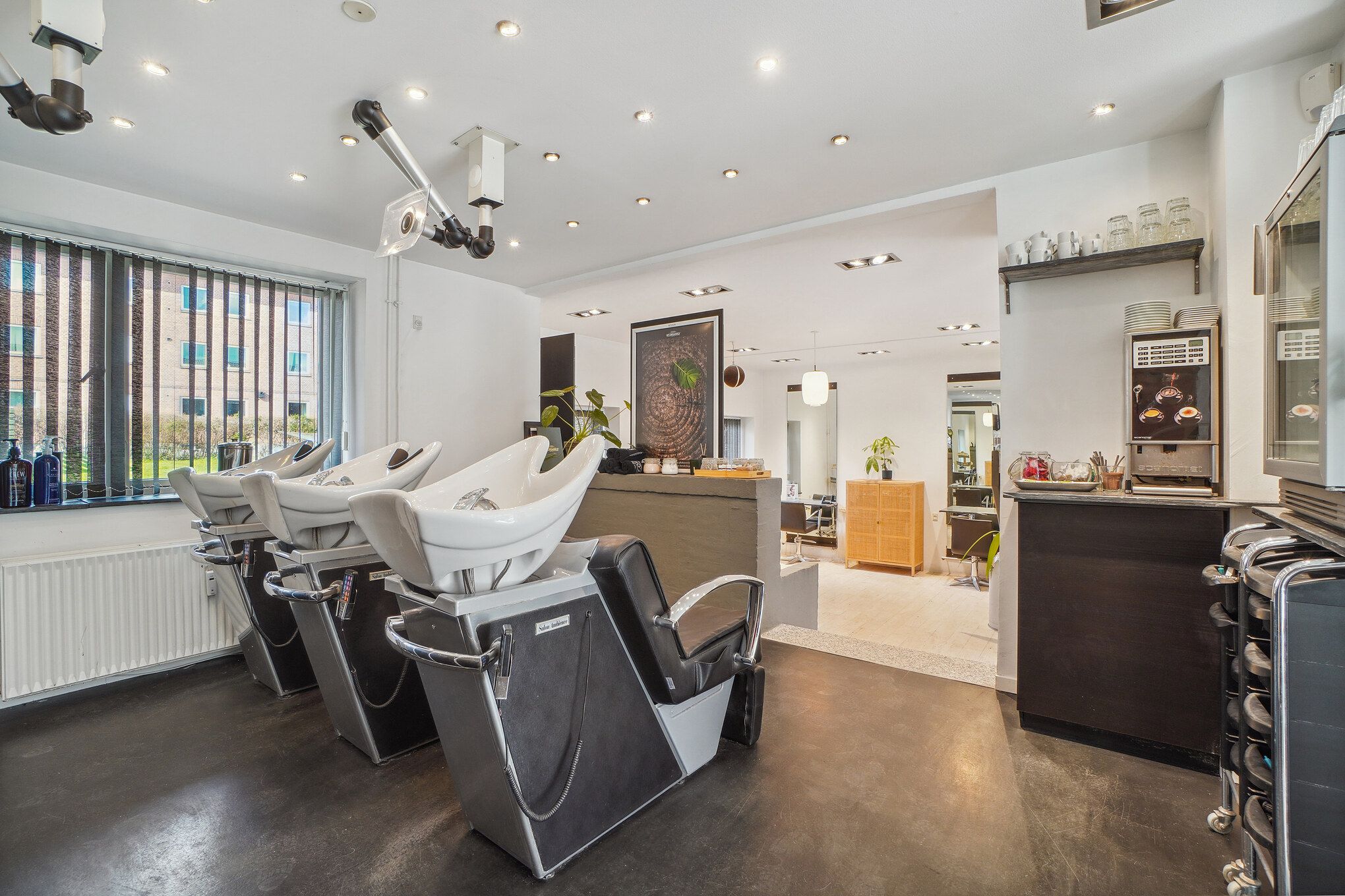 Ny frisørsalon med højt belyste lofter, moderne salonstole, og højt udstyrede salgsområder, inklusive en kobling til