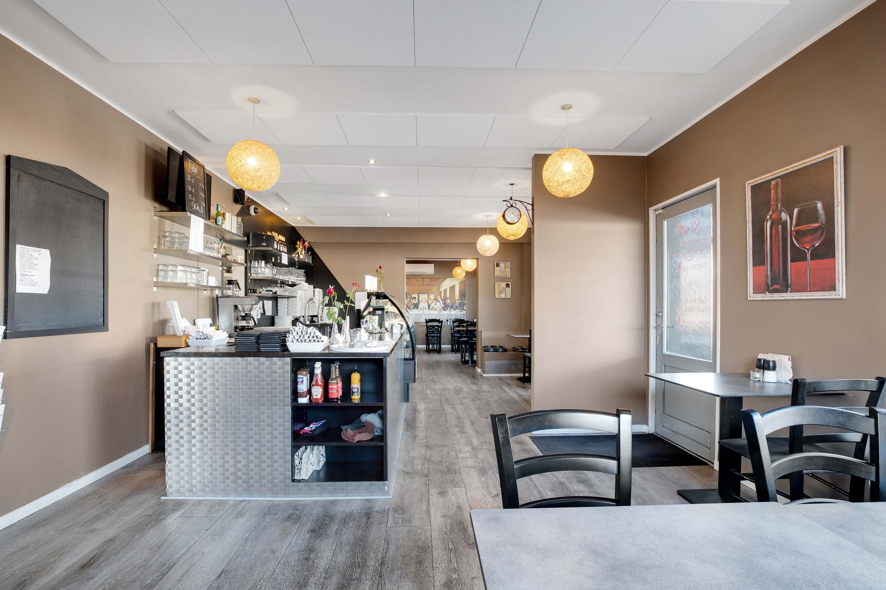 En moderne restaurant med lysegult loft, hvide vægge og gulv og møbler i dyb sort og grå. Der er en bar med flasker og en