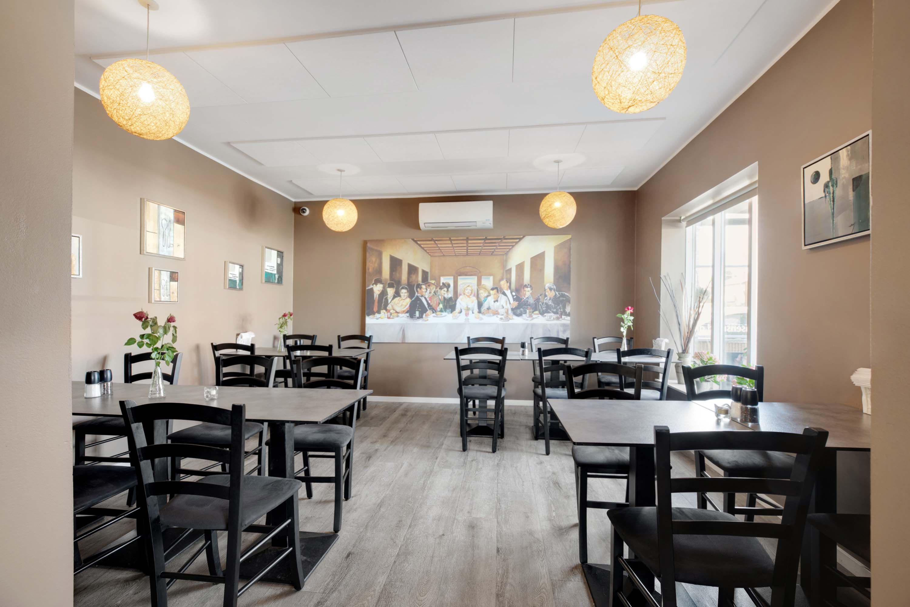 Restaurant med runde, hængende lamper, moderne indretning og en stor maleri på væggen.