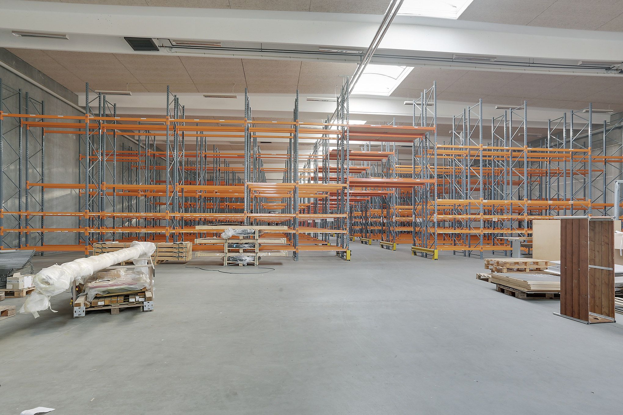 Et stort lager med mange orange og grå hylder samt flere stel og paller fordelt på gulvet
