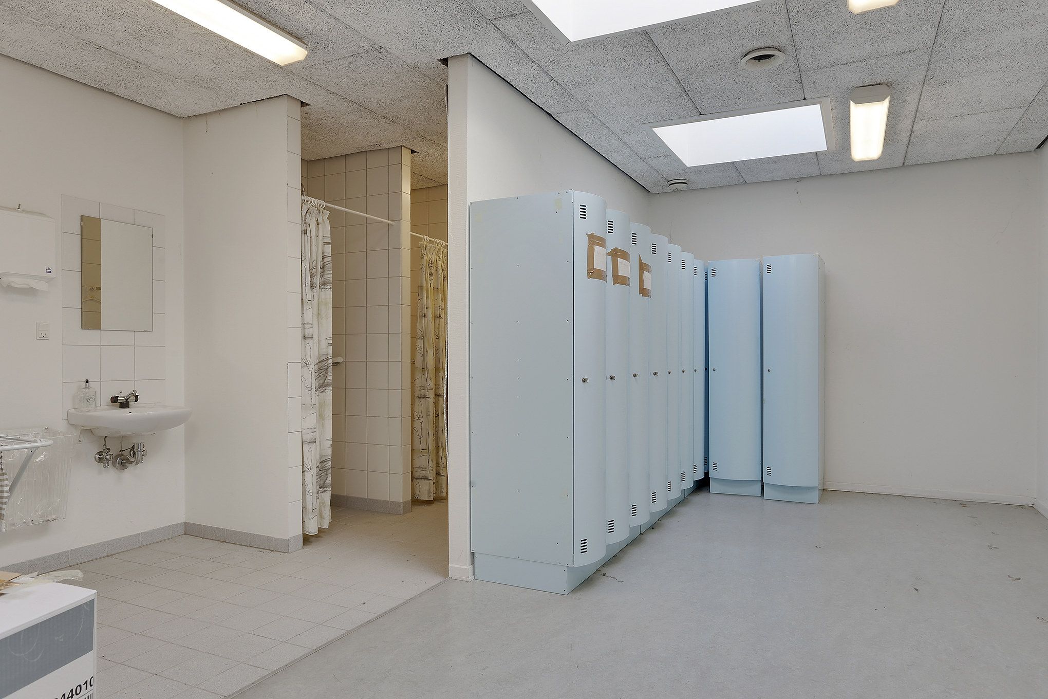 To toiletrum med toiletpapirudgiver og håndvask og fire luksuriøse toiletkabiner med håndklædeholdere og en duschkabin med