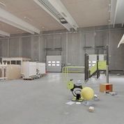 Et stort rum med store hvide loftsbjælker og gulv samt to store døre og gulvmonteret udstyret til produktion