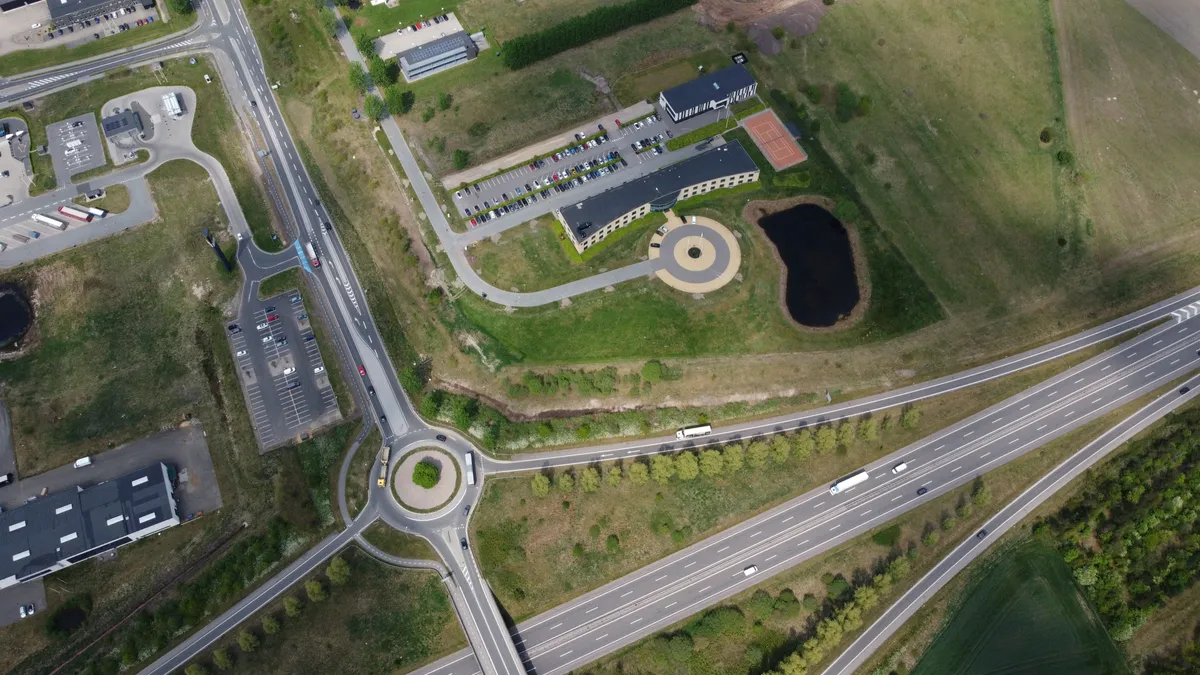 Luftfoto af en parkeringsplads og et sving på en motorvej med biler og lastbiler i begge retninger