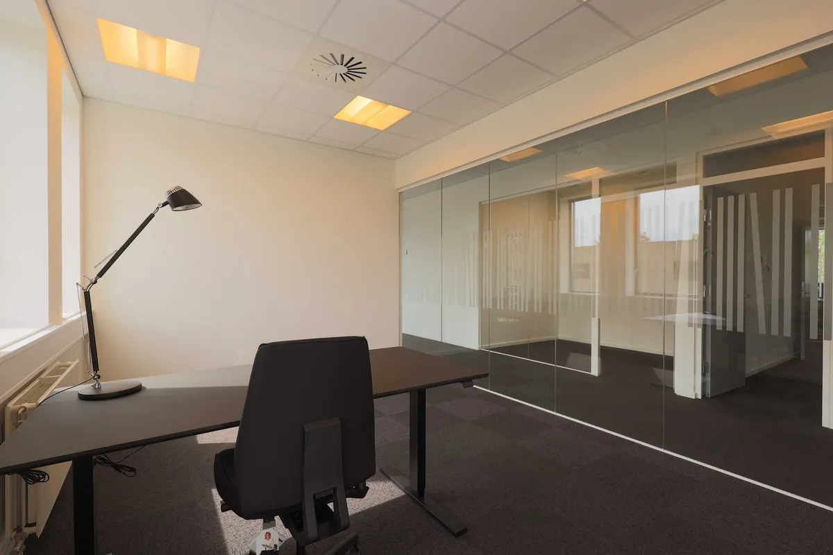 En moderne kontor med glasvægge og et sort bord med en lampe og en stol i en hjørne.