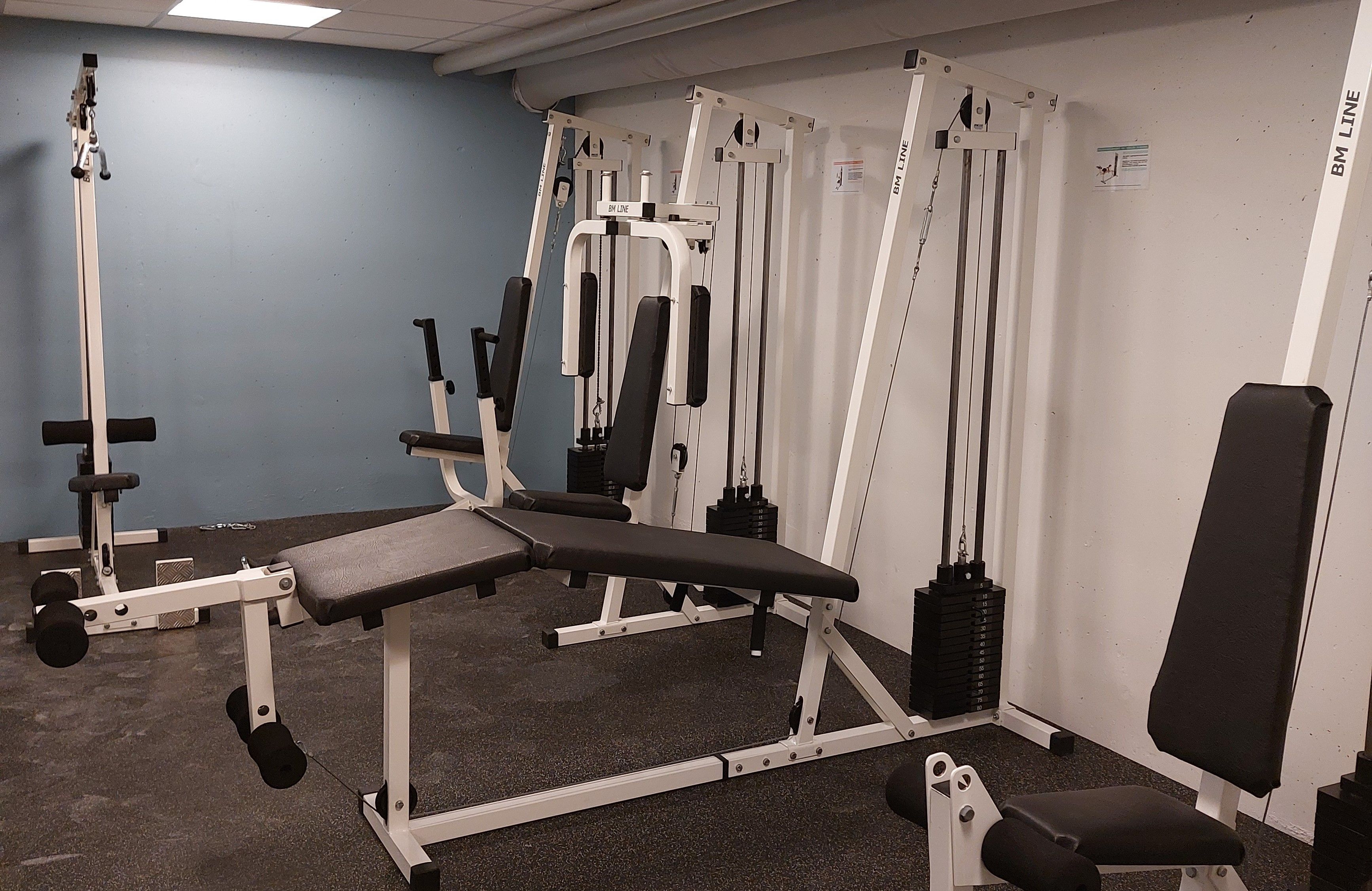 Billede af en simpel fitnesslokale med træningudstyret som en løftemaskine, sæde, håndvægte og træningshåndtag