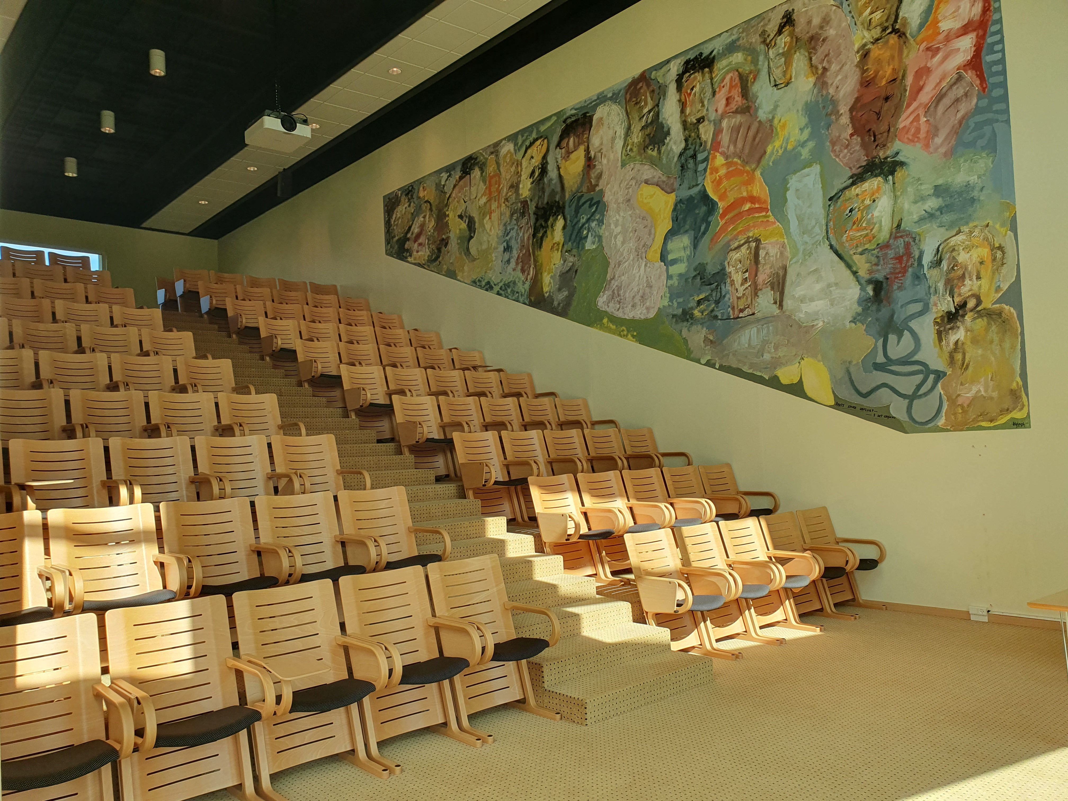 Rækker med lyse og moderne kontormøbler uden folk i salen med billedvæg og projektor