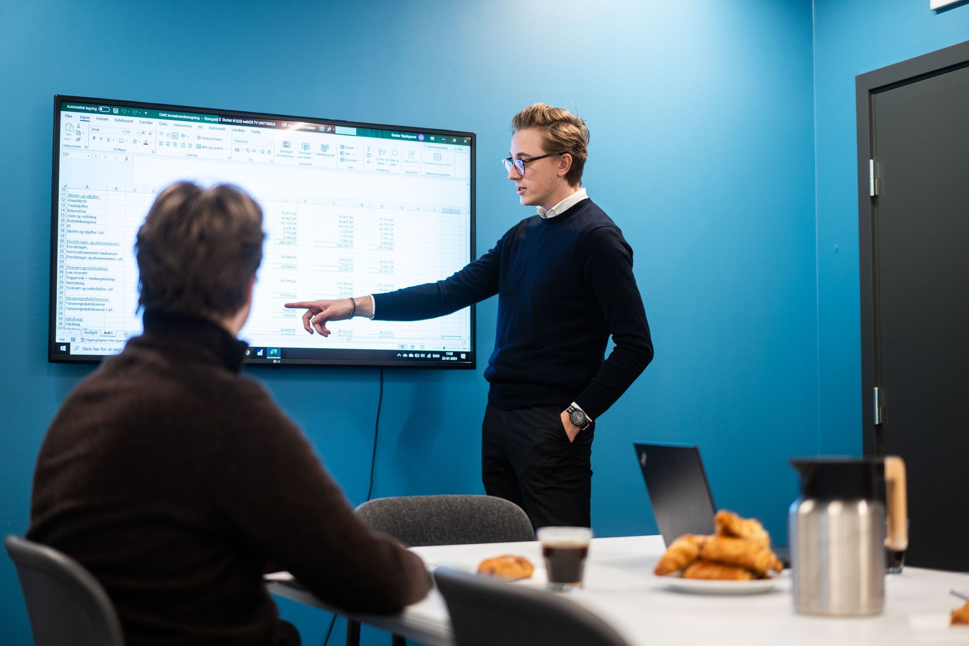 To mænd i kontor læser regneark på monitor og spiser croissanter og drikker kaffe