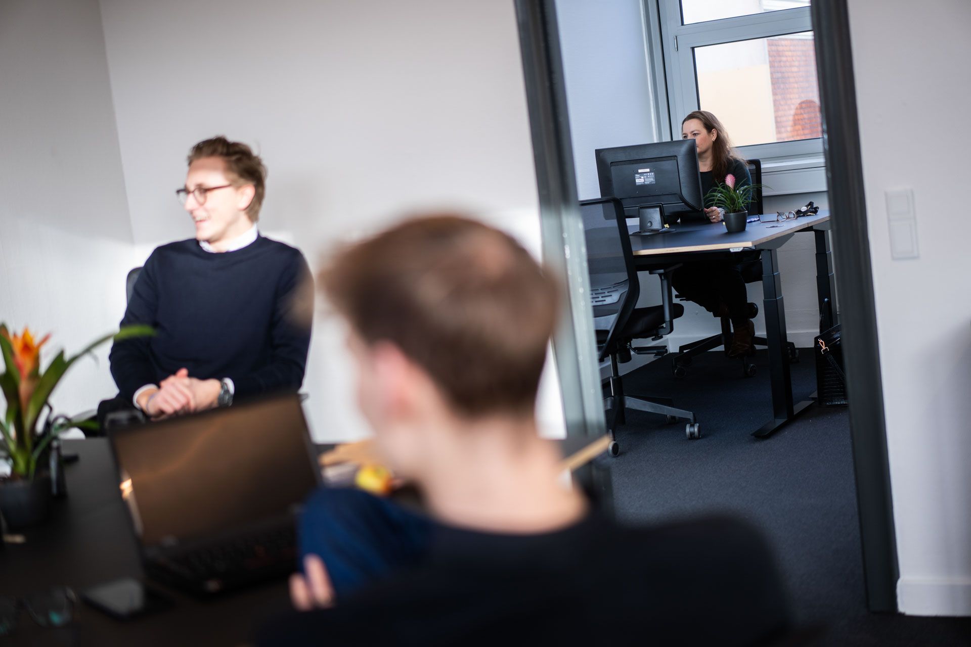 To mænd og en kvinde sidder i en kontor med lyse vægge og højt til loftet