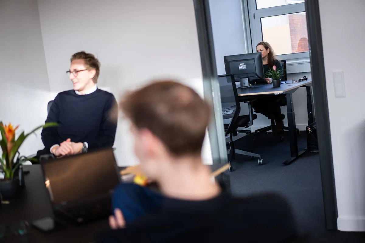 To mænd og en kvinde sidder i en kontor med lyse vægge og højt til loftet