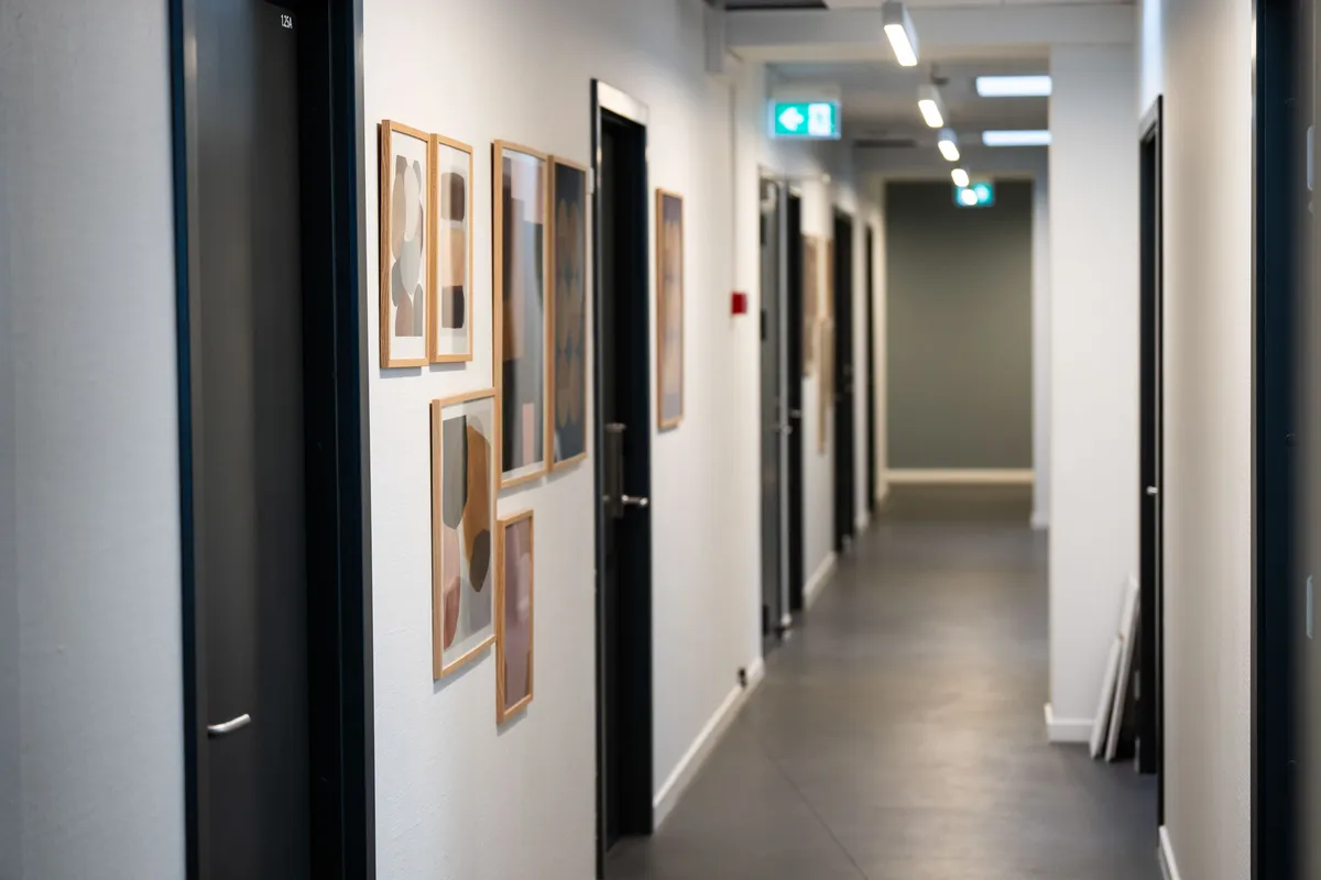 Langt korridor med åbne døre og kunstværker på væggen og lysekroner i loftet
