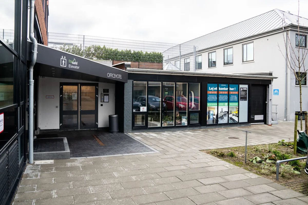 Privatkontor til leje, indgang med elevatorskilt og forretningslokaler med glasvinduer og parkerede biler