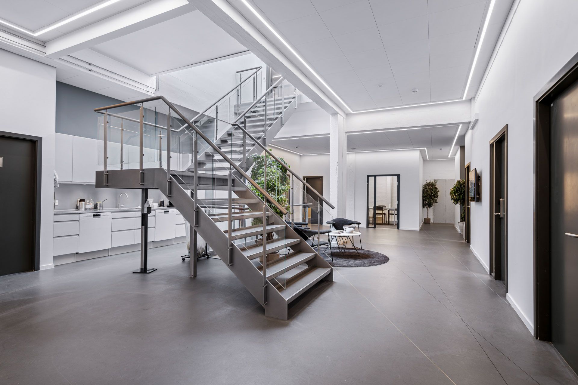 Et moderne, rent og minimalistisk kontor med en stor, glasklædt trappe og en møbleret lobby med en række komfortable møbler