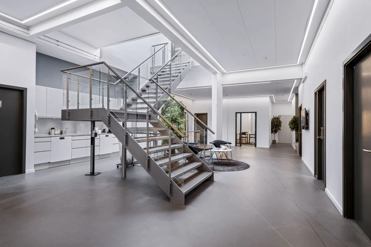 Et moderne, rent og minimalistisk kontor med en stor, glasklædt trappe og en møbleret lobby med en række komfortable møbler