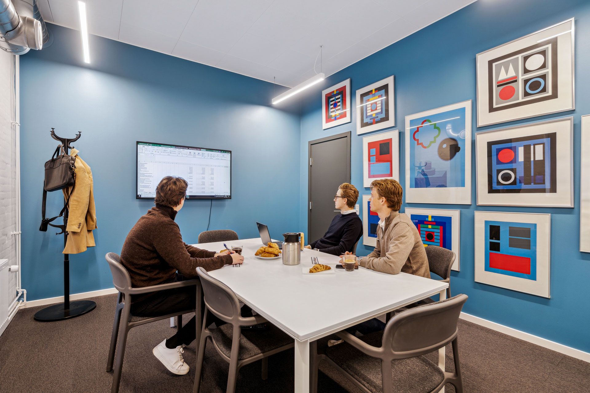 Gruppe af mennesker sidder rundt om bordet og taler i et kontor med lyseblå vægge og kunstværker