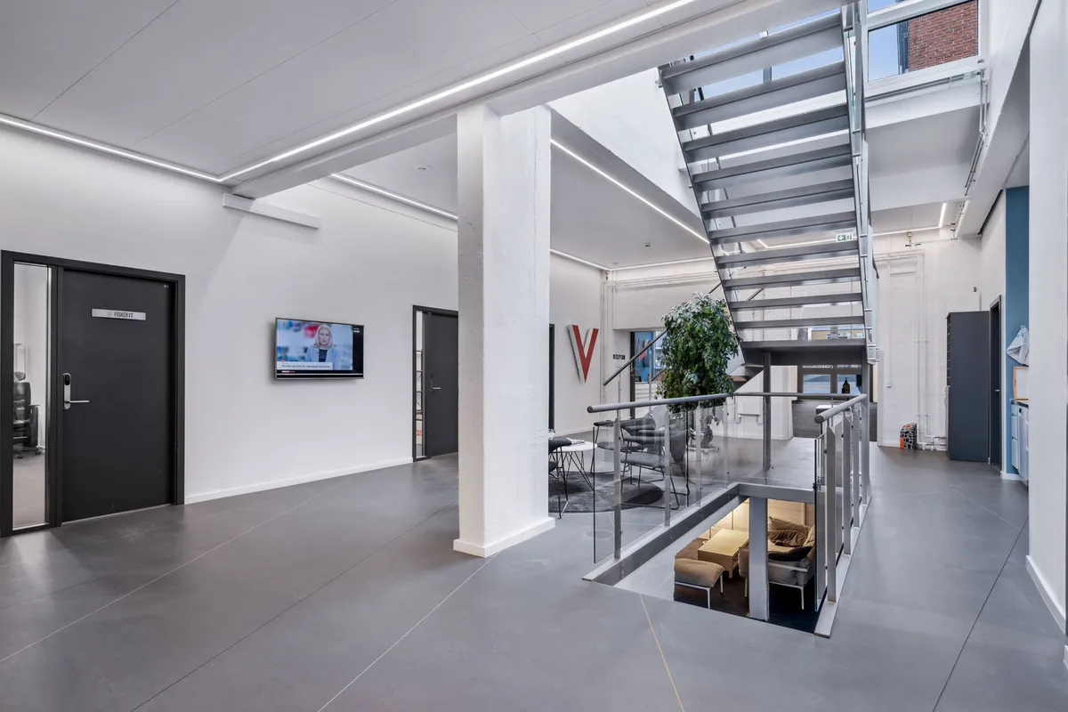 En kontorlokal med en TV-skærm, et skrivebord og en stige med et højdekammer med en sofa