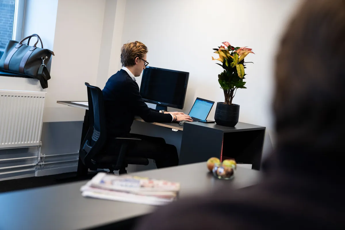 Man sidder i et kontor med en laptop og en større skærm i baggrunden