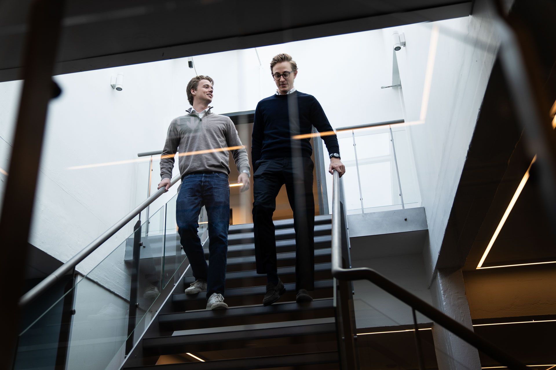 To unge mænd går op ad trapperne og holder hver deres håndled i håndtaget på det glasbelægningsråd af trappen