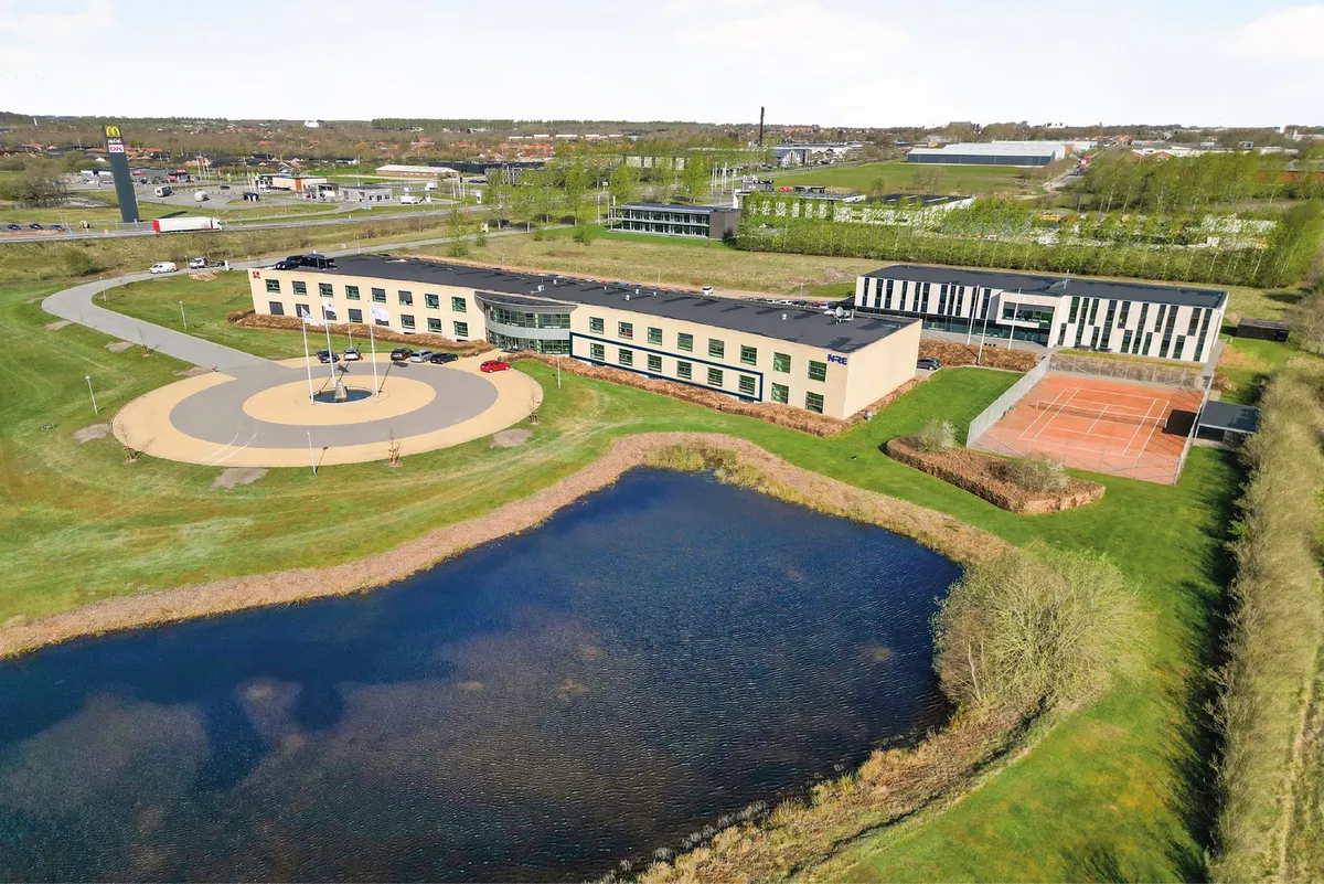 Moderne bygning med en tennisbane, parkeringsplads og en McDonald's-restaurant i baggrunden. Bygningen er omgivet af en stor
