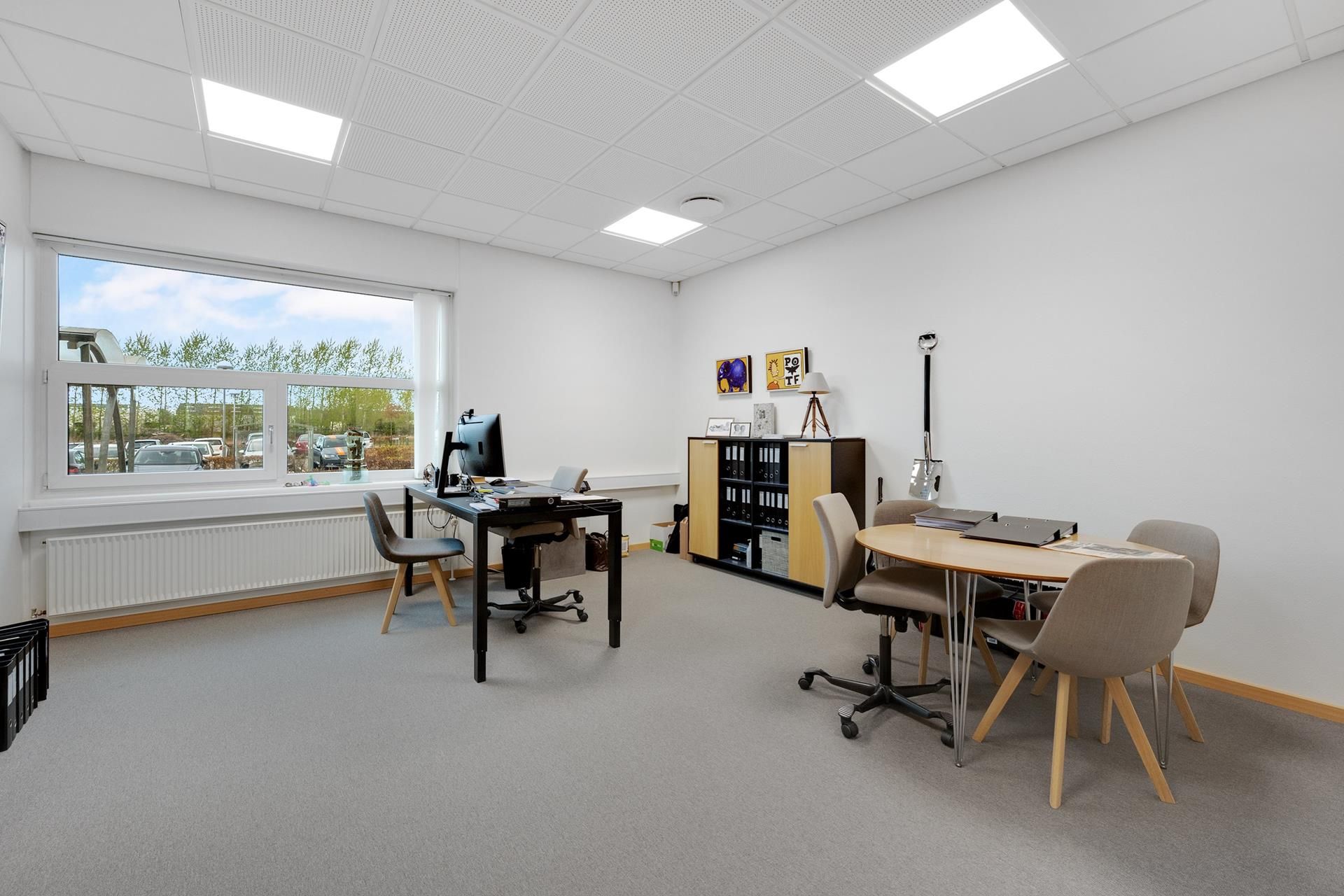 En kontormøbleret med skrivebord og computer samt et lysegult skrivebord med fire stole