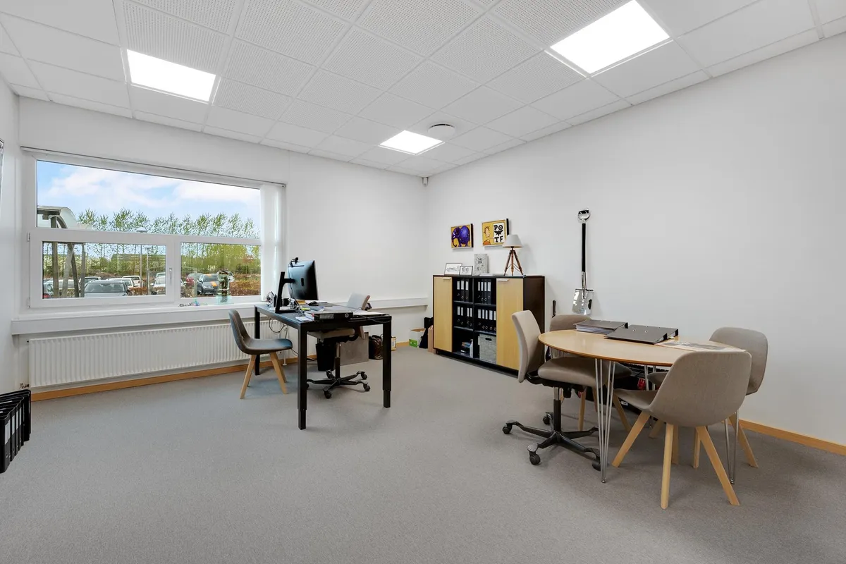 En kontormøbleret med skrivebord og computer samt et lysegult skrivebord med fire stole