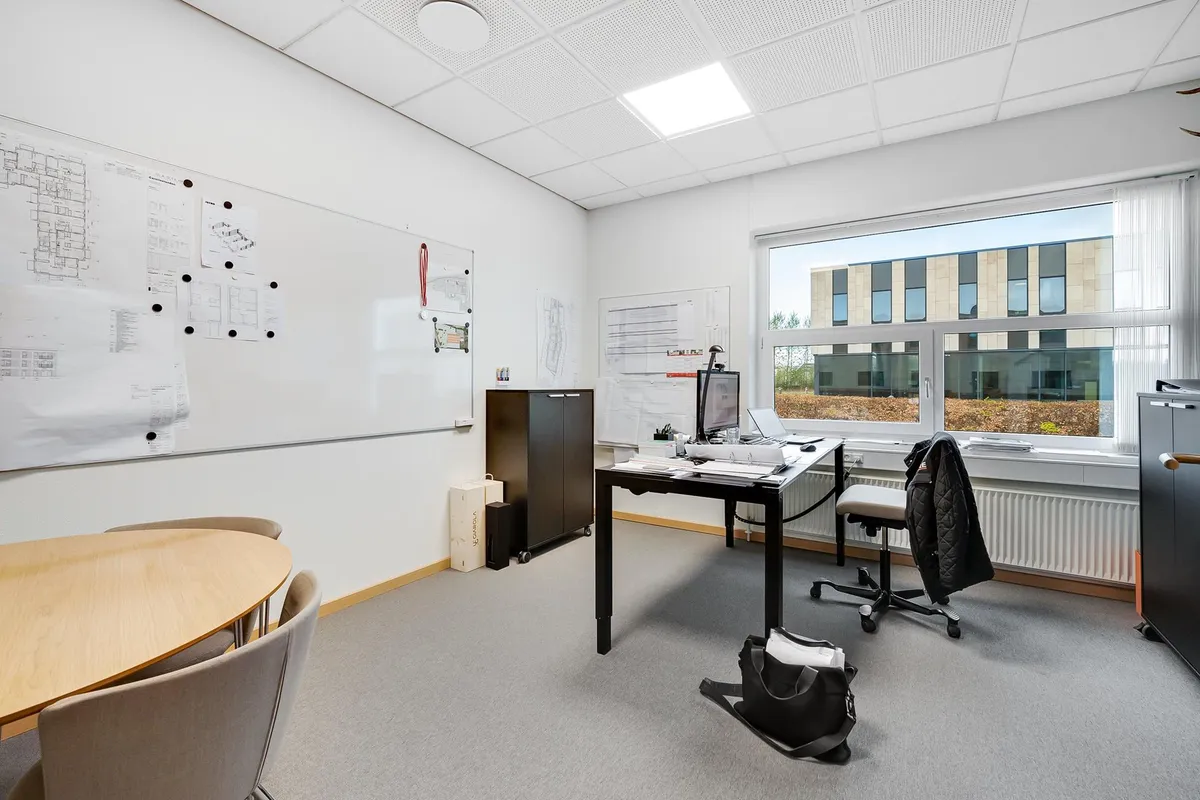 Kontor med bord, skrivebord og stol med klædeskab, stol med jakke og hængsel. Ovre er der et skrivebord og en computer med