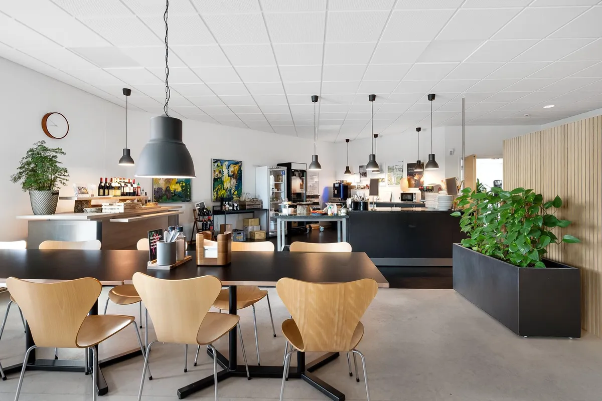 Et moderne kontor med lyse lofter, høj gulvfinish og møbler i lysebrunt. Bord og stole omkring en central serveringsstation.