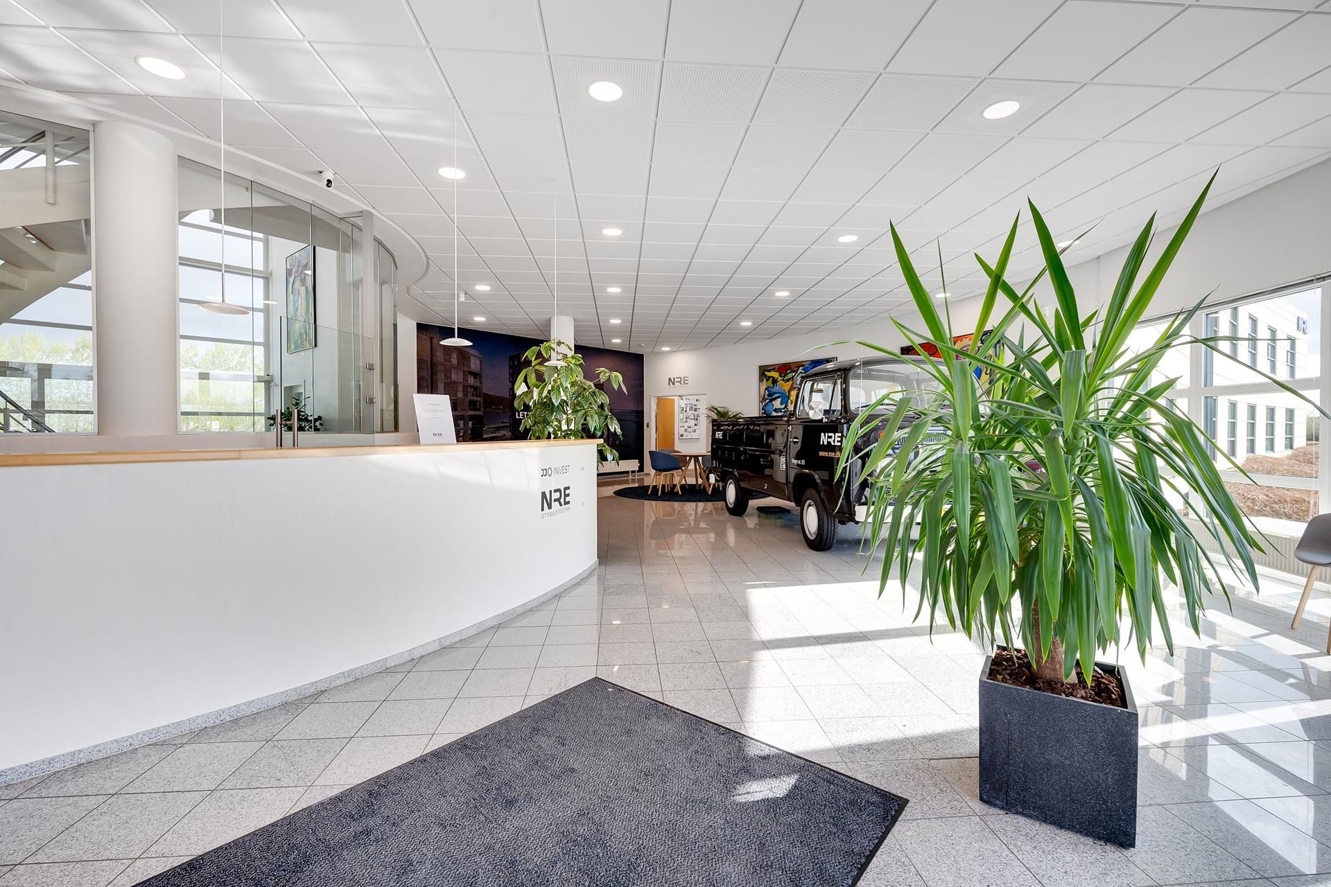 Vidunderligt kontor med hvid marmorgulv og store glasruder med udsigt til byen. Der er en stor plante og et gammelt køretøj