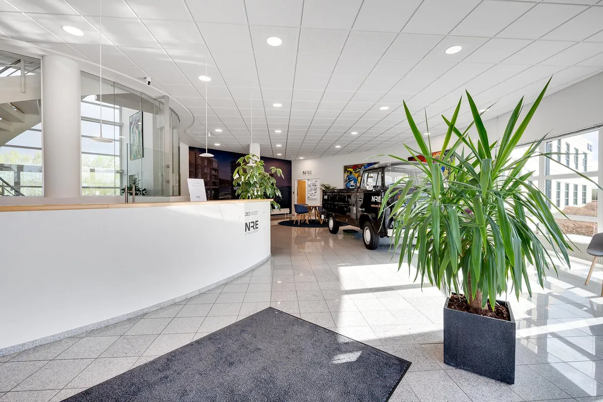 Vidunderligt kontor med hvid marmorgulv og store glasruder med udsigt til byen. Der er en stor plante og et gammelt køretøj