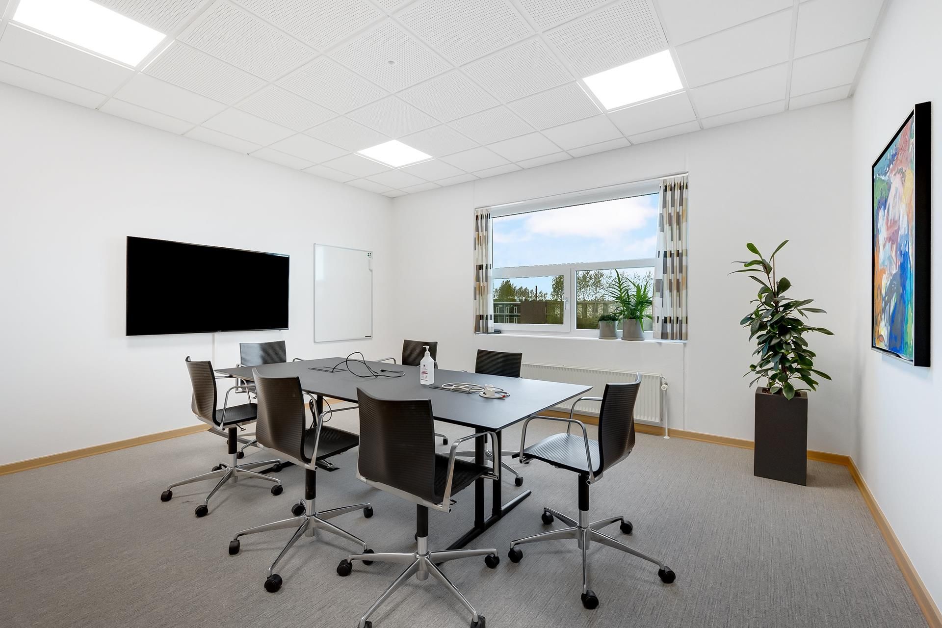 Kontor med lysekrone, tv, skrivebord, stole, tæppe, plante og vinduer med gardiner i hvid, grå og grøn farve