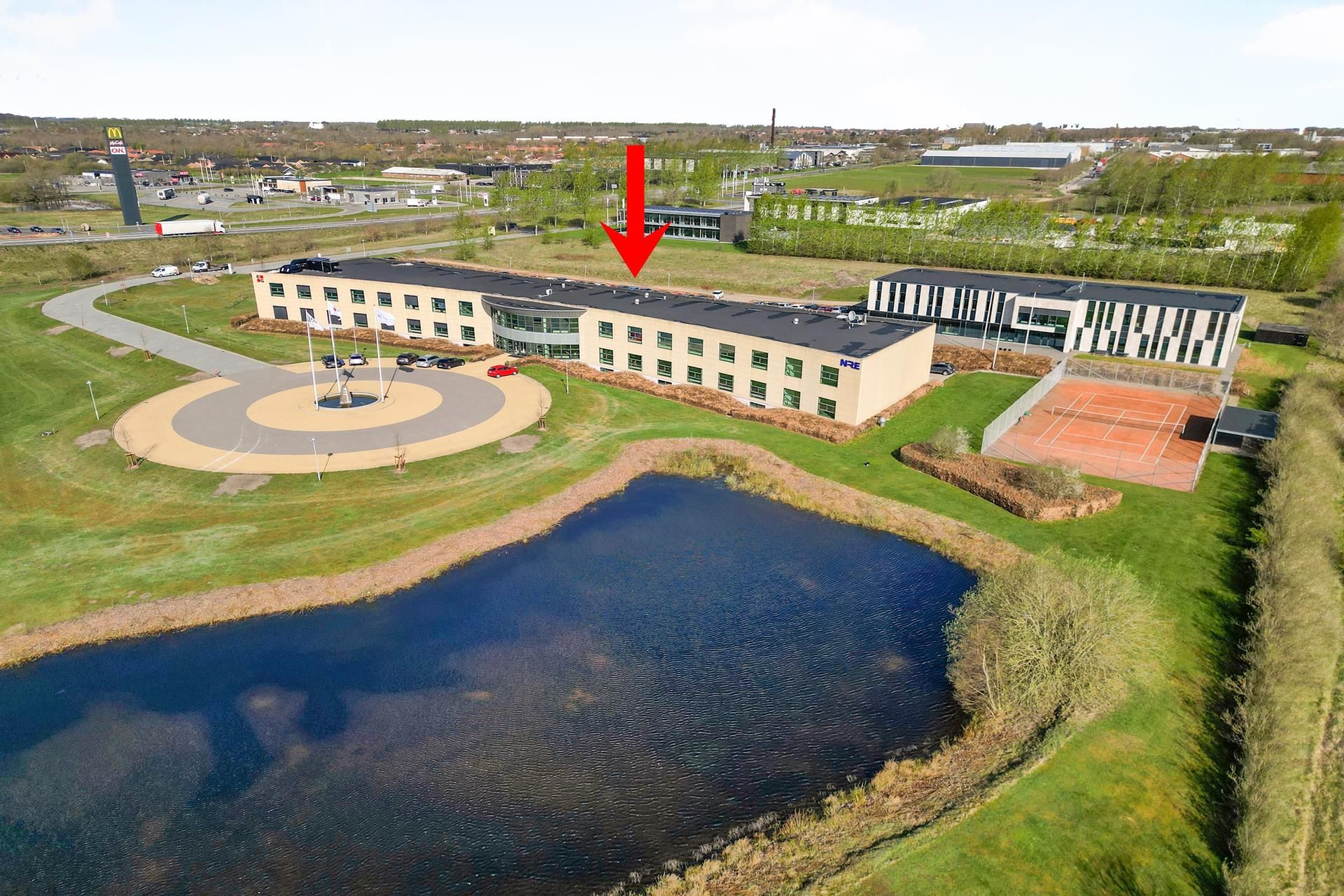 En moderne bygning med facade mod motorvejen med en tennisbane og sø med udsigt mod Herning og Aarhus