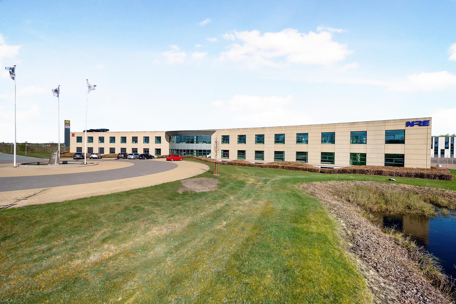Store kontorbygning med teksten NRE i blåt og to McDonald's flag på høje flagpole. Foran bygningen er en grøn plæne med en