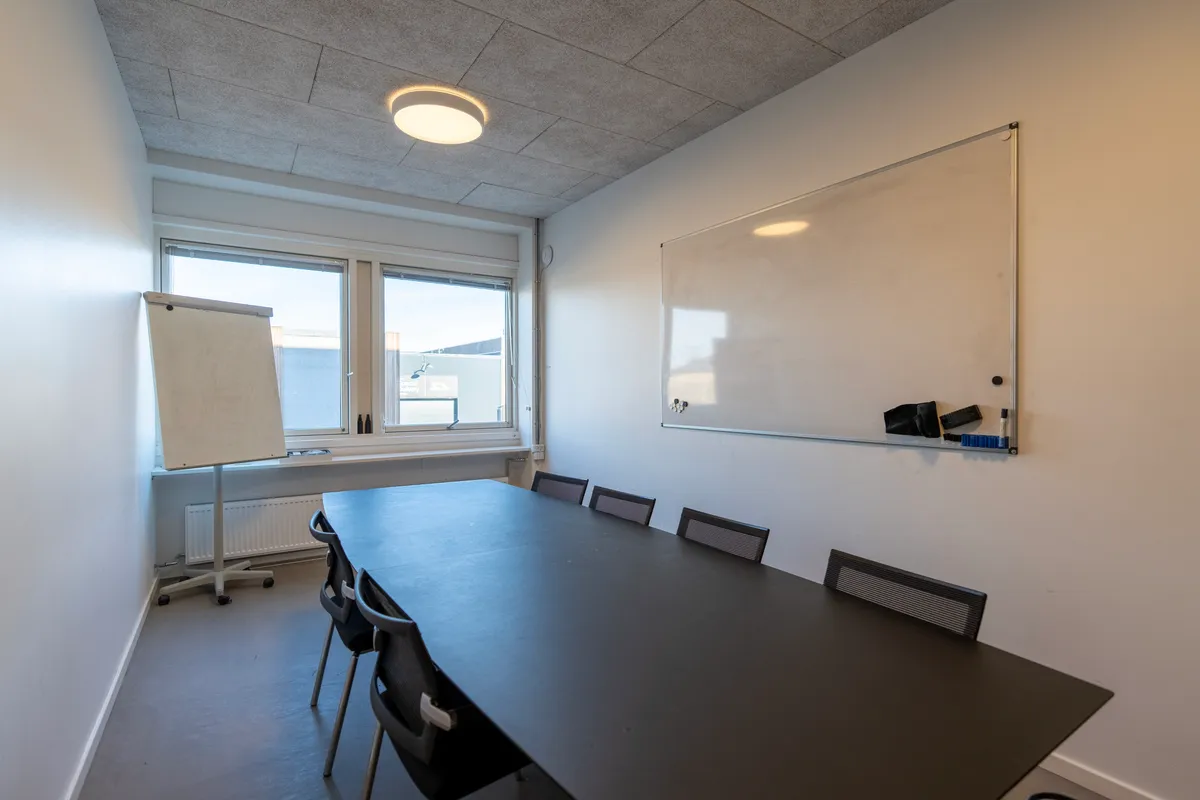 Kontor med mødebord og stole samt et whiteboard og en hvid væg med en magnetbord