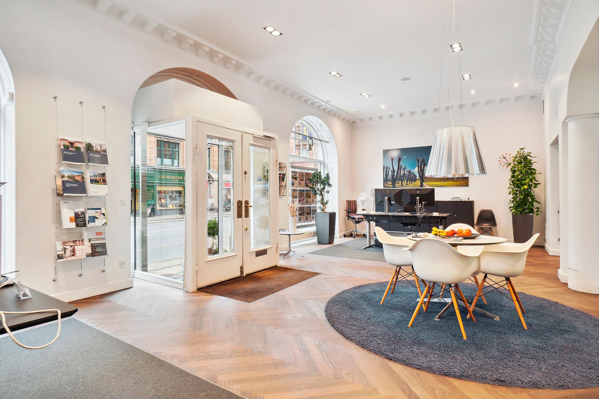 Elegant og veludstyret boligkontor med højt til loftet og lyse hvide vægge. En stor rund gulvmåtte og fire hvide stole med