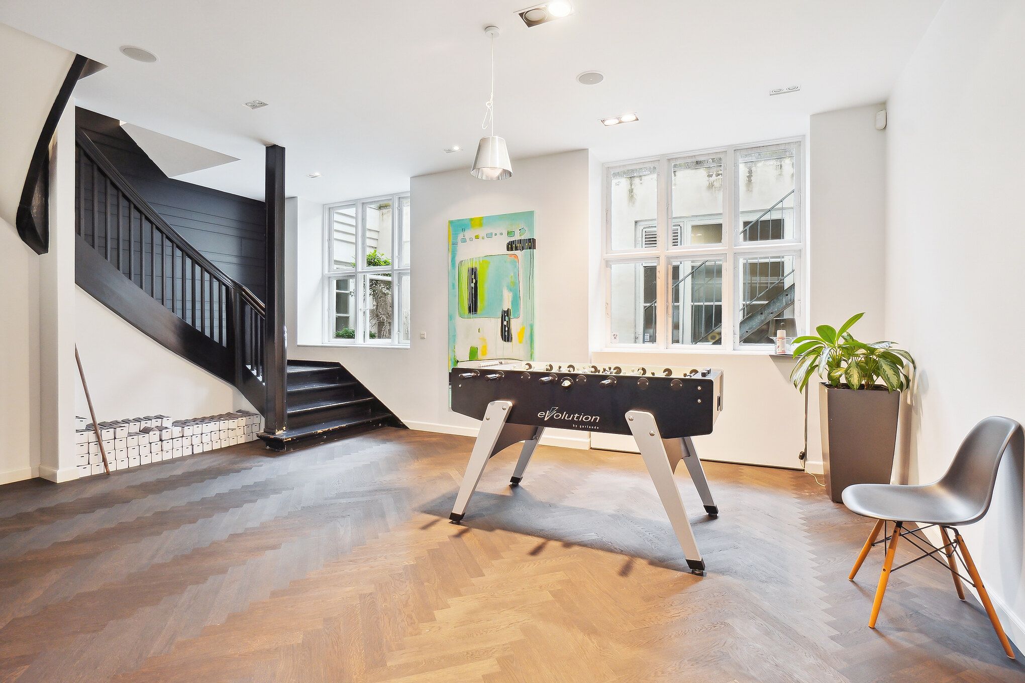 En stor stue med et højt loft, en stor træfodbold og en stol samt en plante på siden